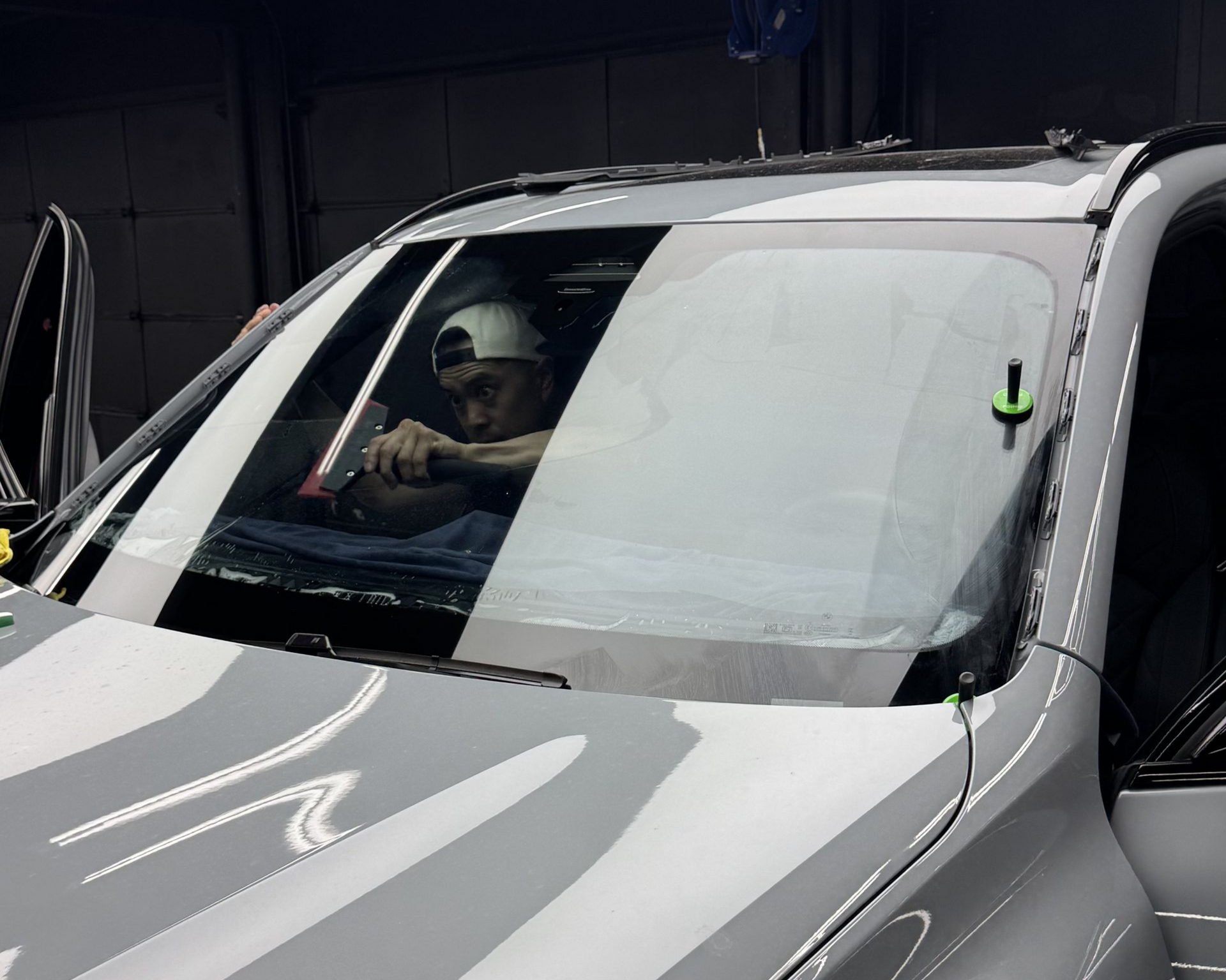 Person inside a silver car seen through the windshield, with the driver door open.