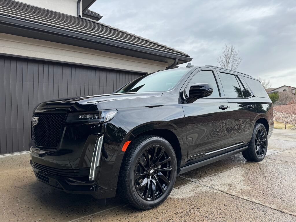A black cadillac escalade is parked in front of a garage.