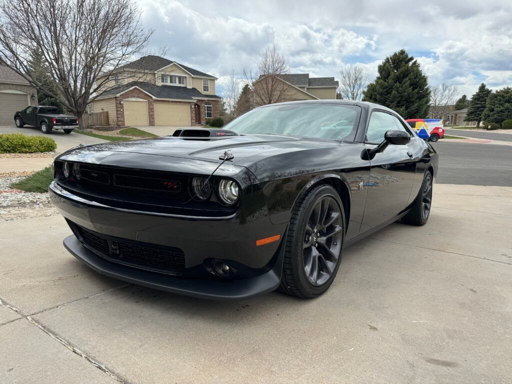 A black dodge challenger is parked in a driveway in front of a house.
