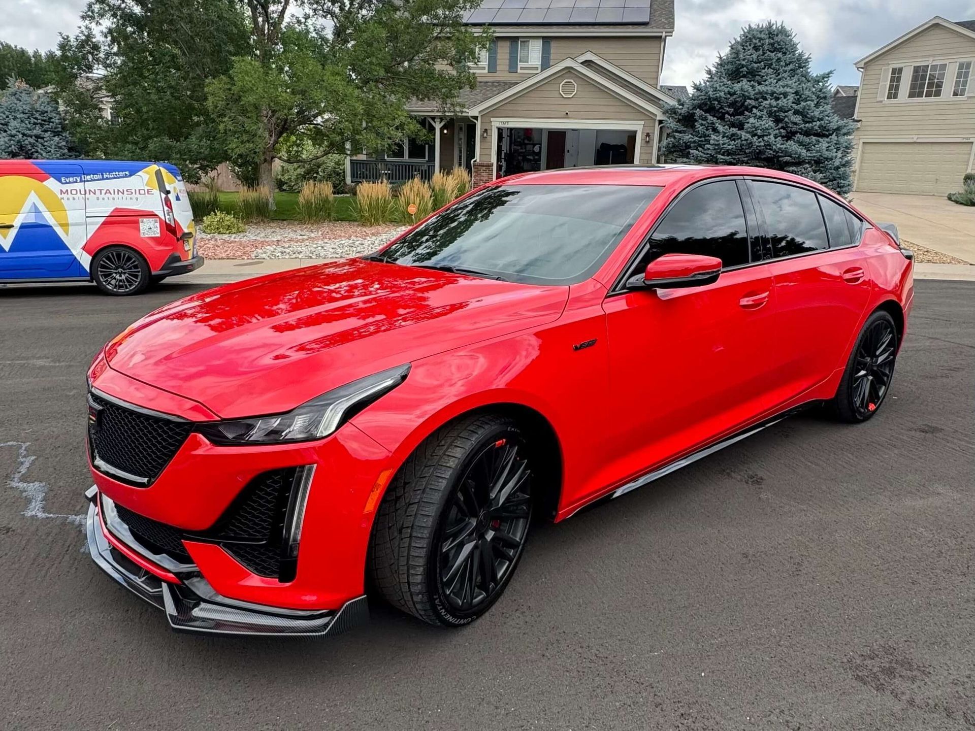 Bright red Cadillac sedan parked in front of a house. It has black wheels and tinted windows.