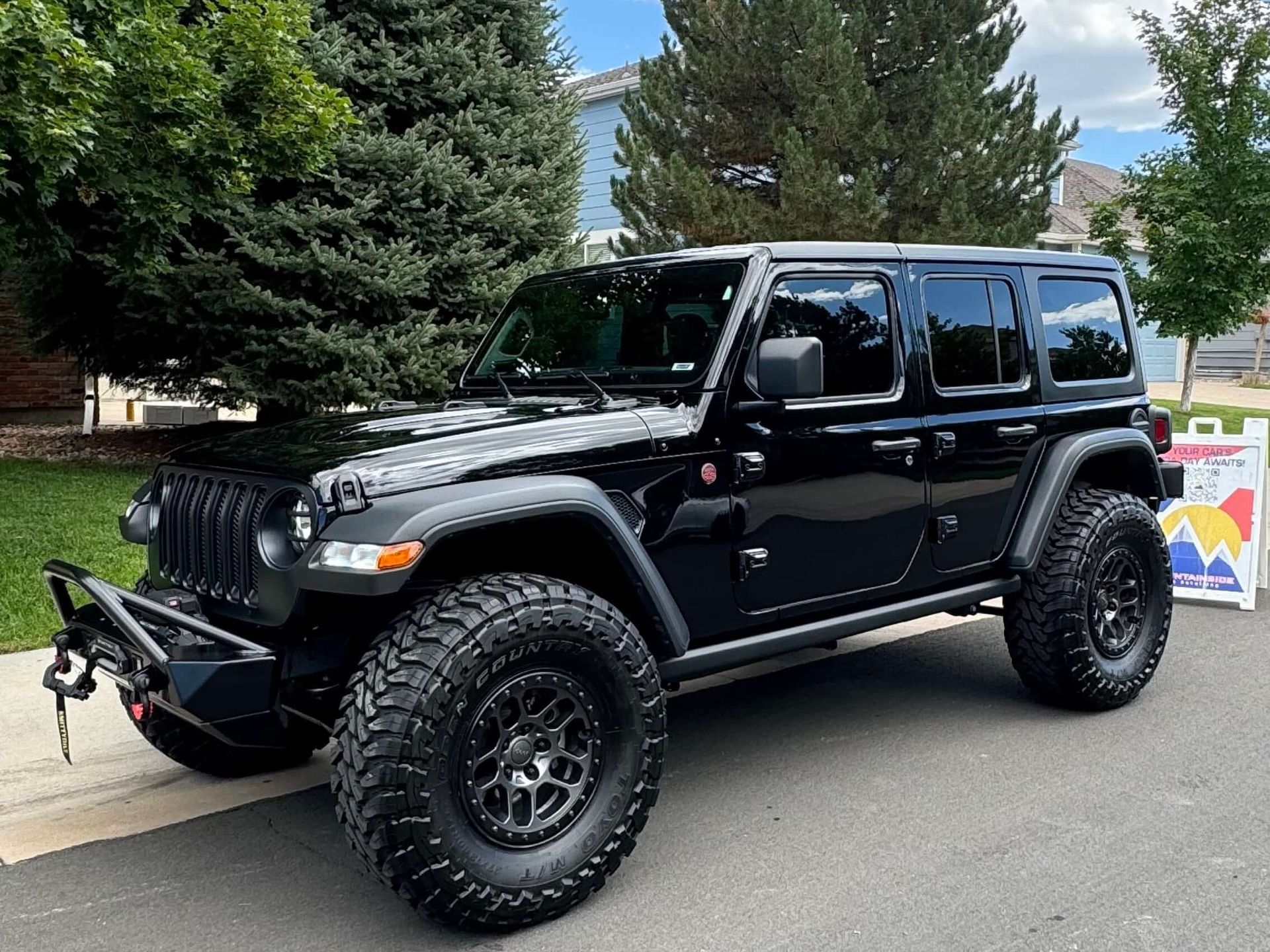 Black Jeep Wrangler parked on a street with large tires, a black front bumper, and tinted windows.