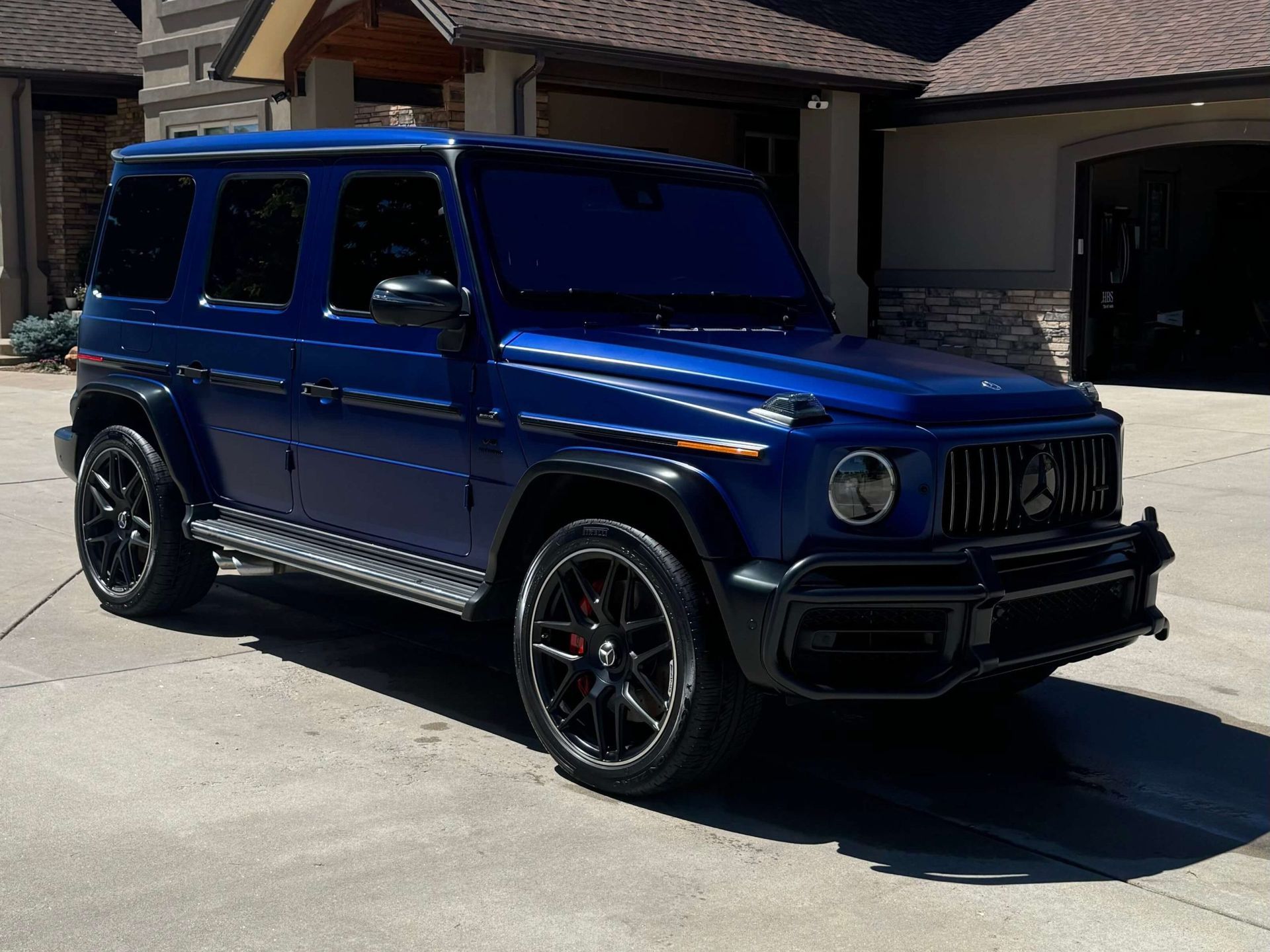 Blue Mercedes-Benz G-Class SUV parked on a driveway in front of a house.