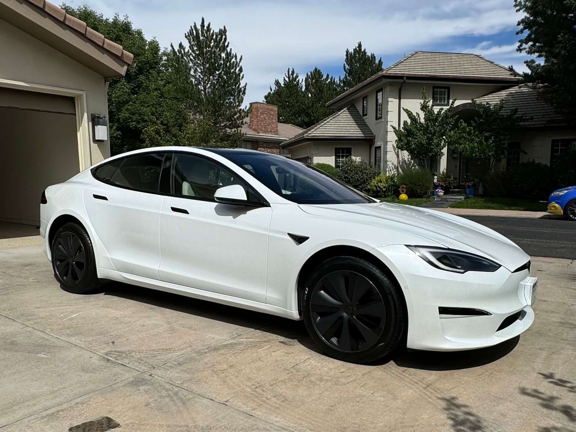 White Tesla car parked in a driveway in front of a house.