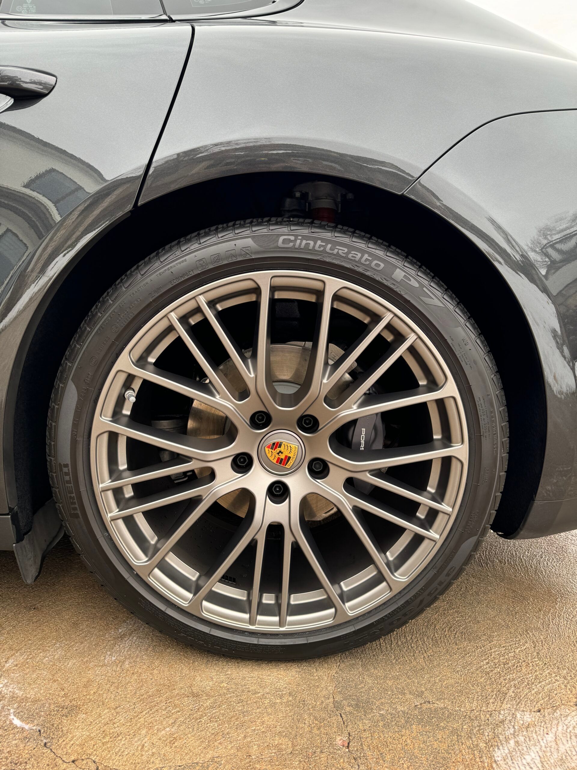 Close-up of a silver alloy wheel with a Porsche logo on a black car.