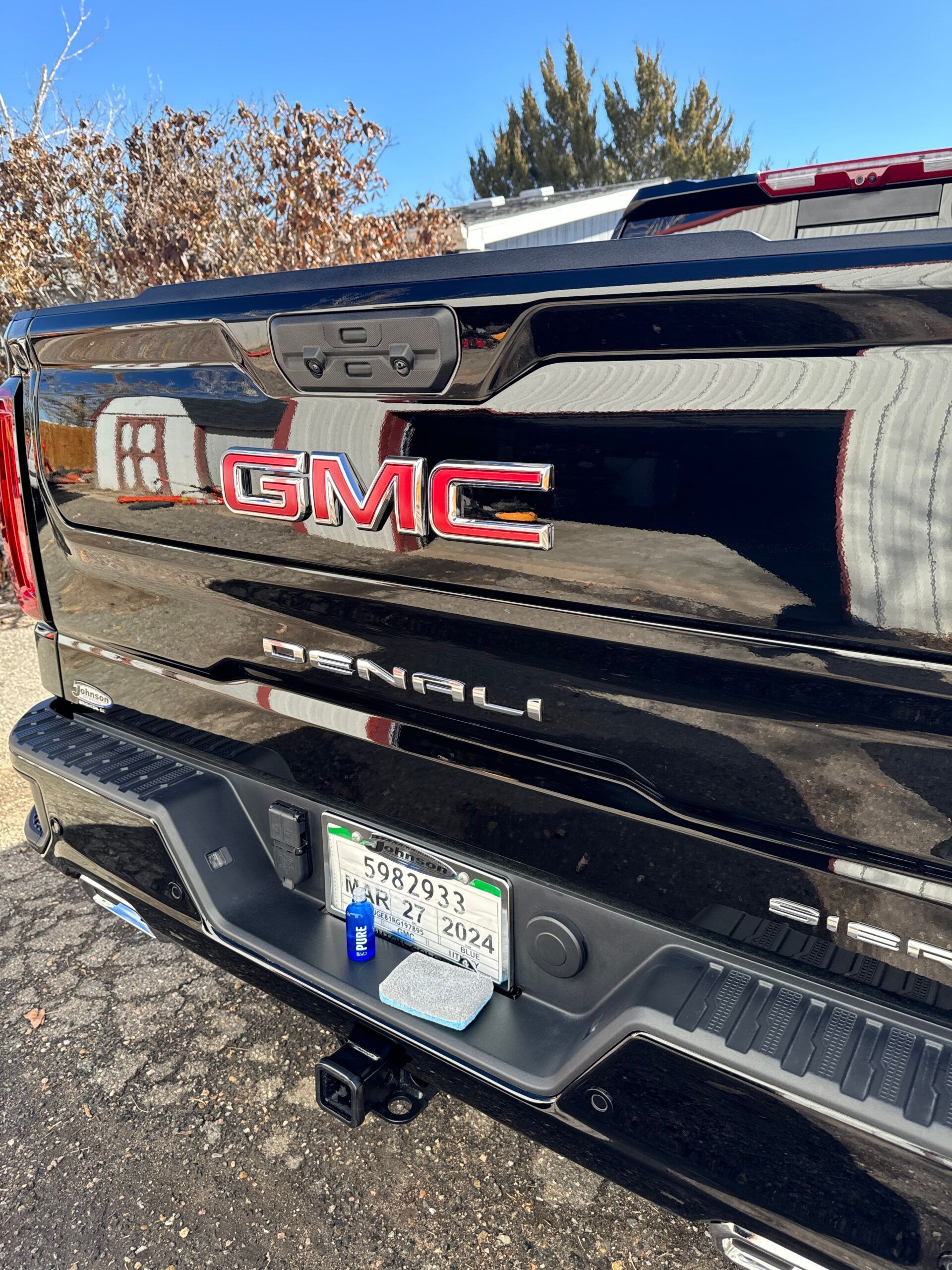 Black GMC Denali truck tailgate with red GMC emblem and license plate. Sunny outdoors.