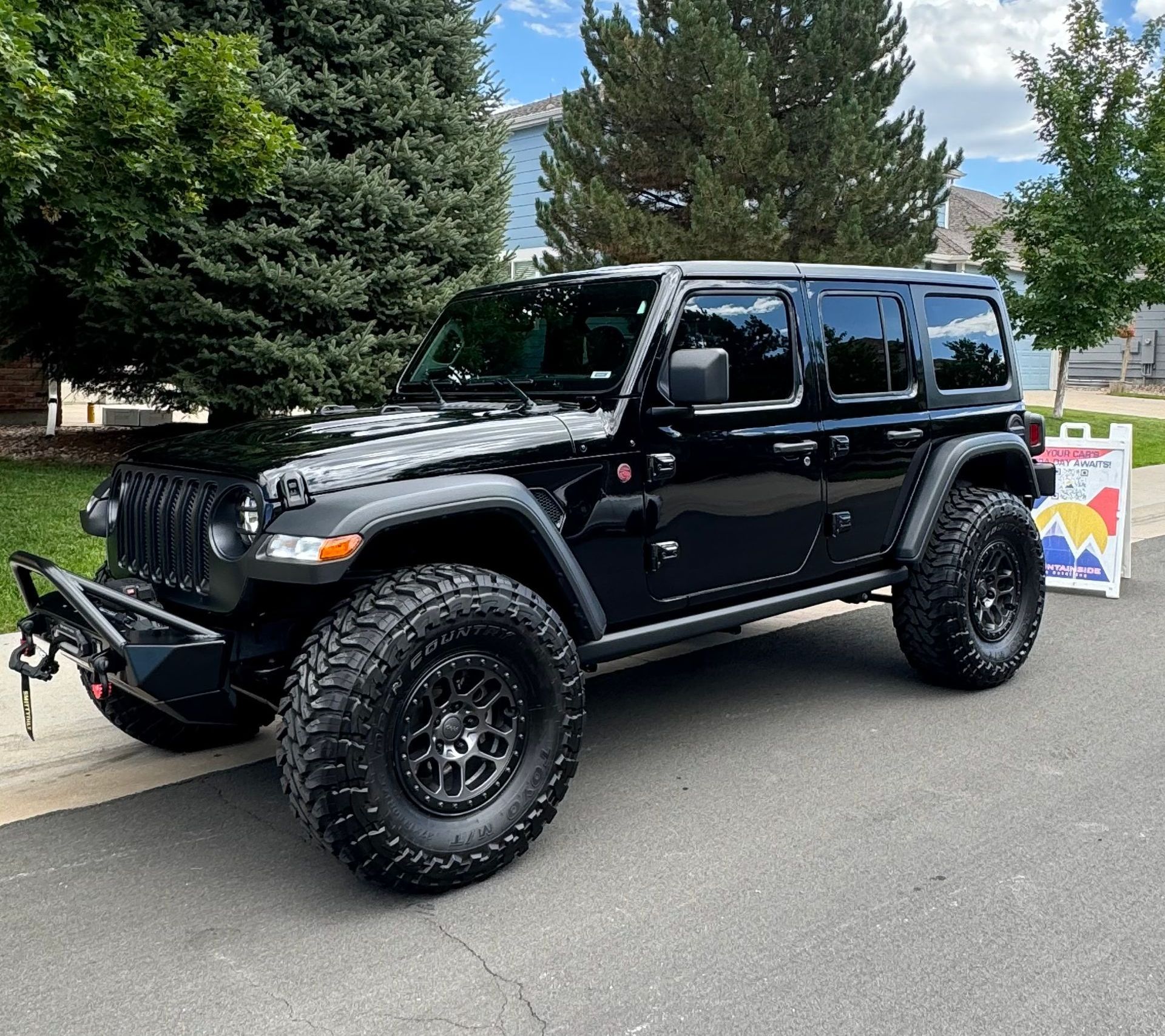 A black jeep is parked on the side of the road next to a sign.