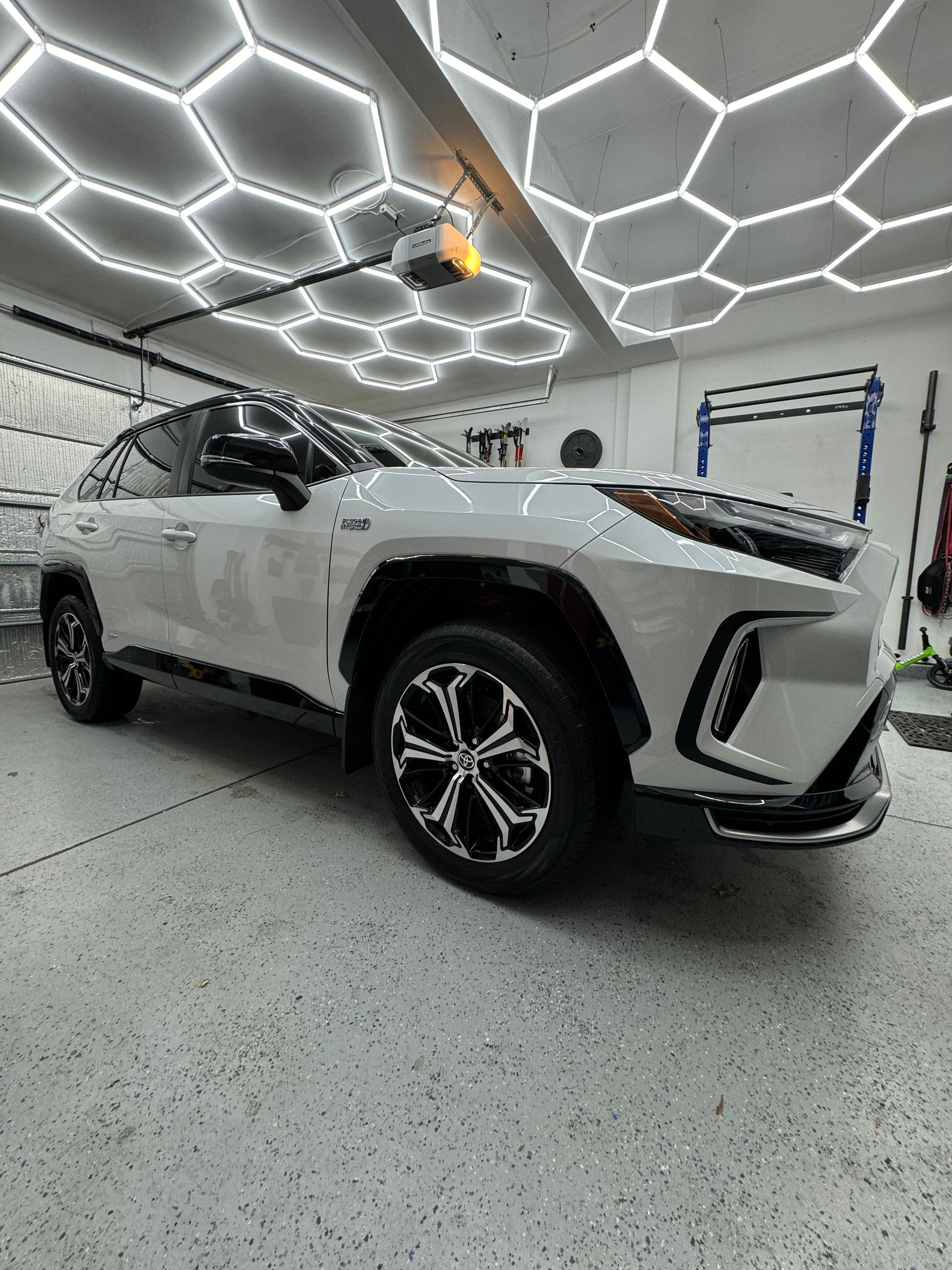A white suv is parked in a garage under a honeycomb ceiling.