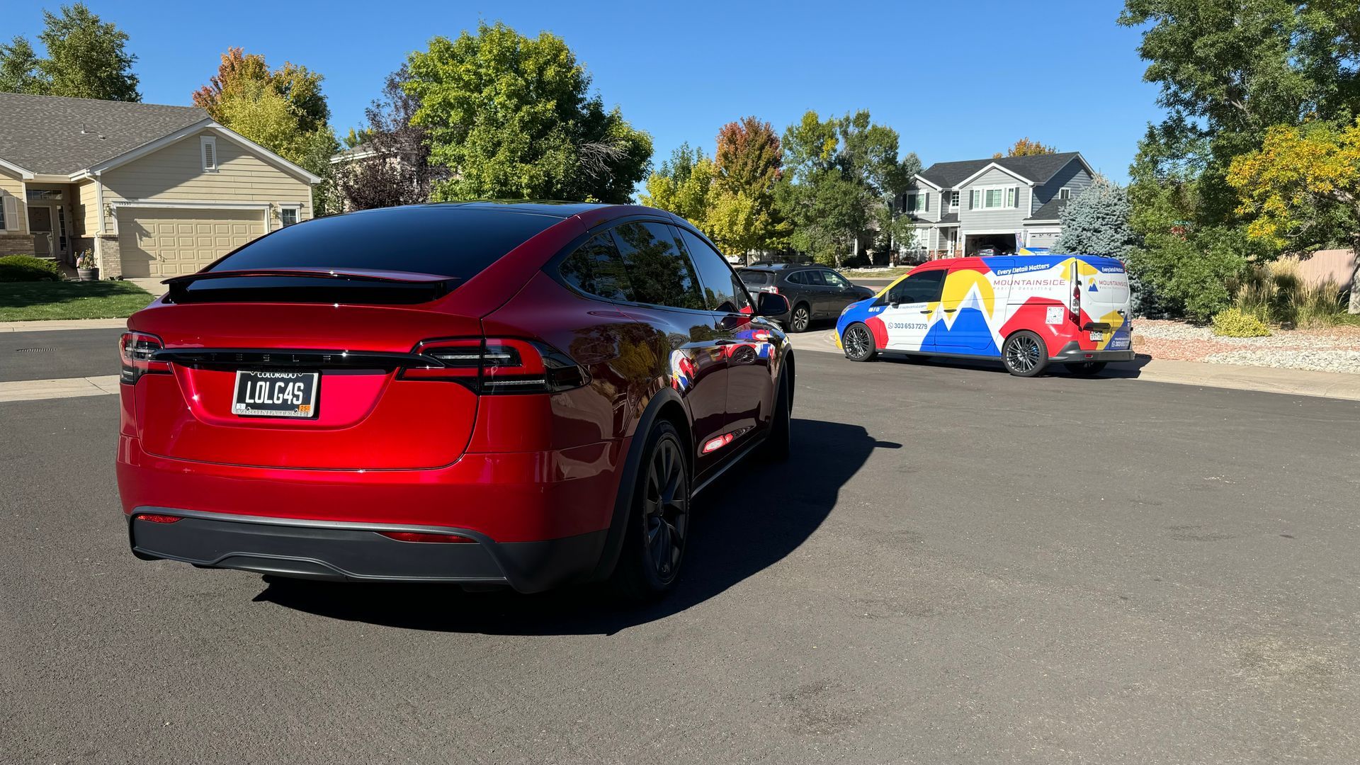A red tesla model x is parked on the side of the road