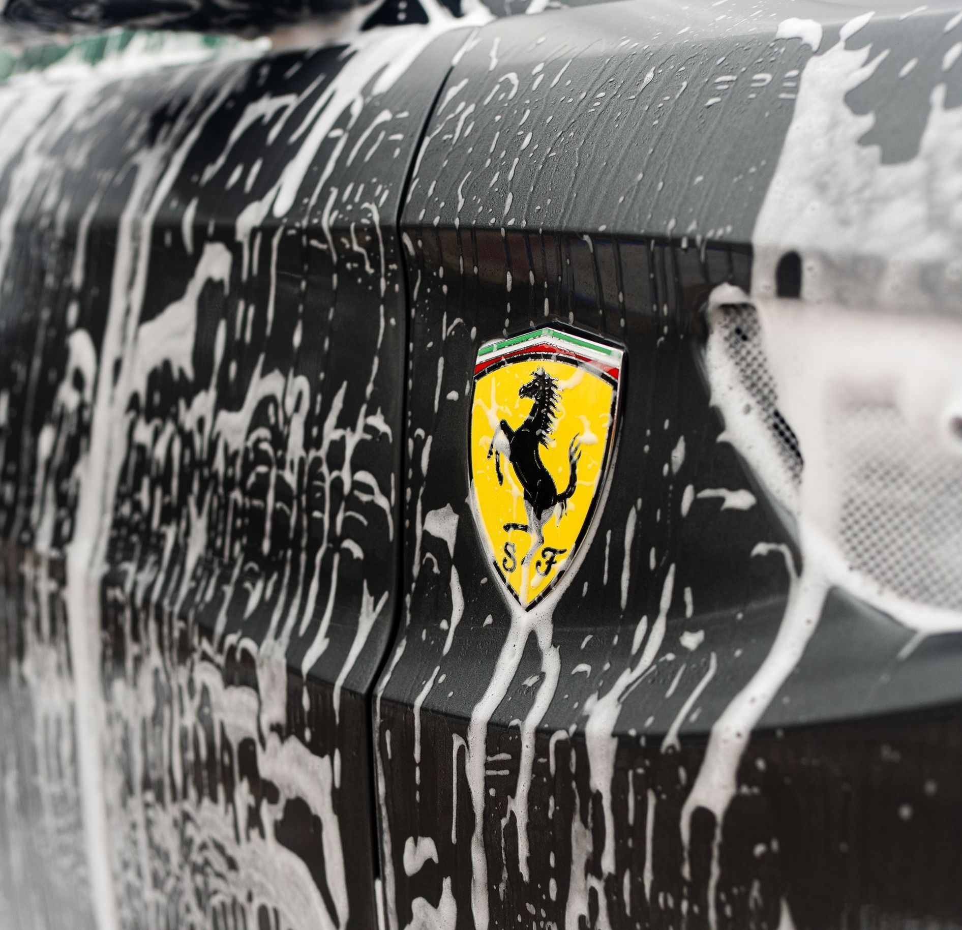 Ferrari emblem on a car door, covered in soapy foam.