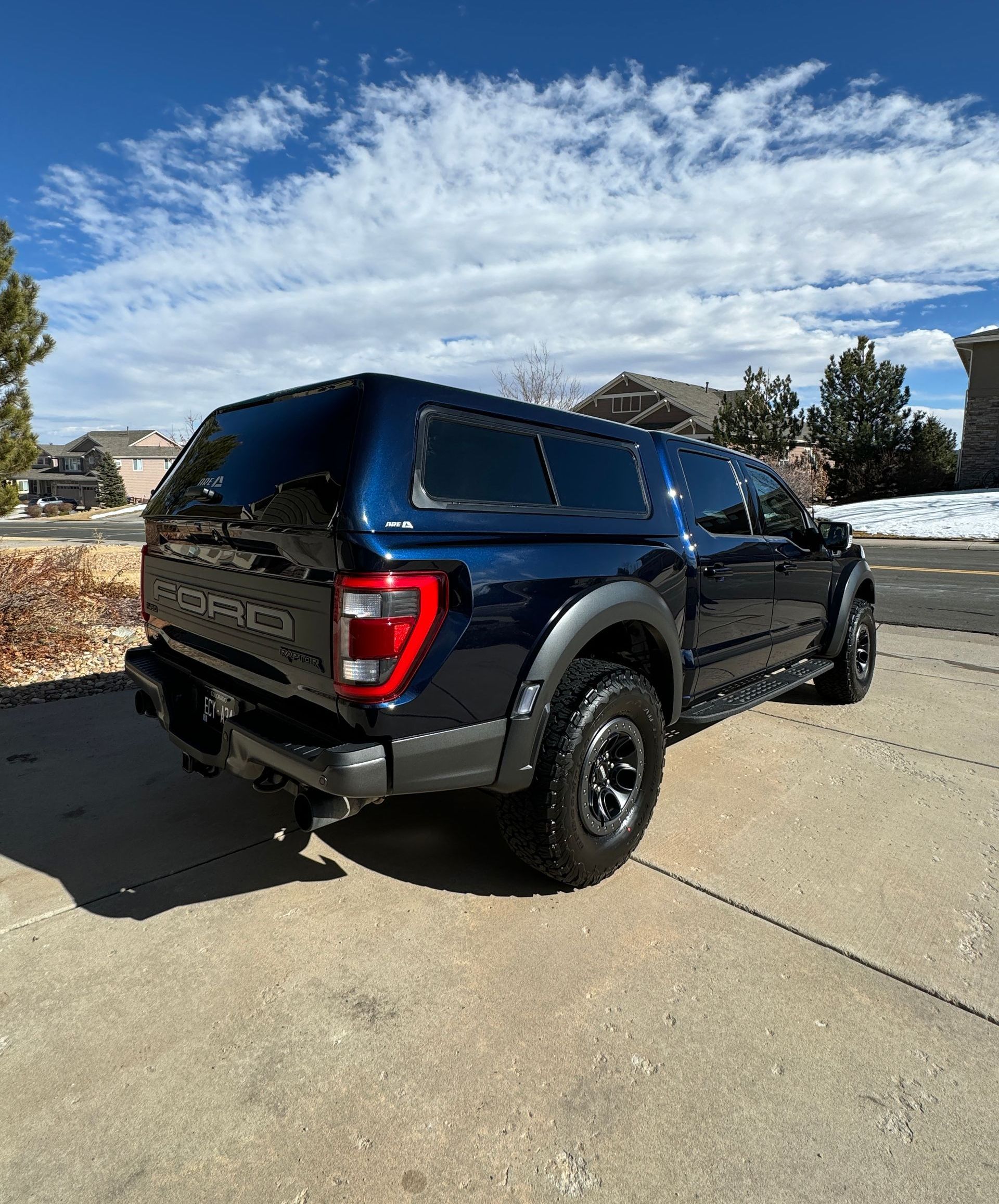 Blue Ford Raptor truck with black bed topper on a sunny day.