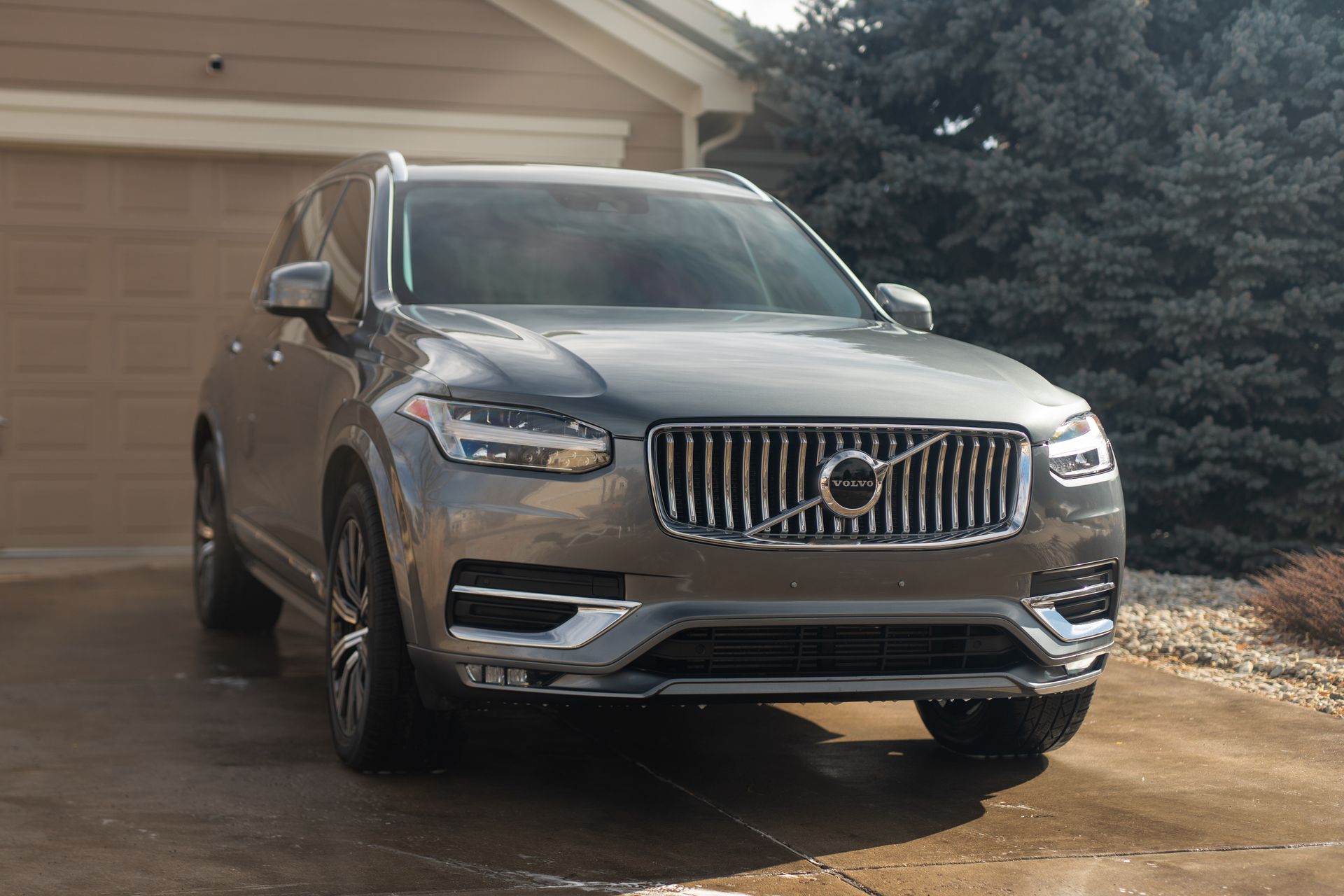 Gray Volvo XC90 SUV parked in front of a garage on a sunny day.