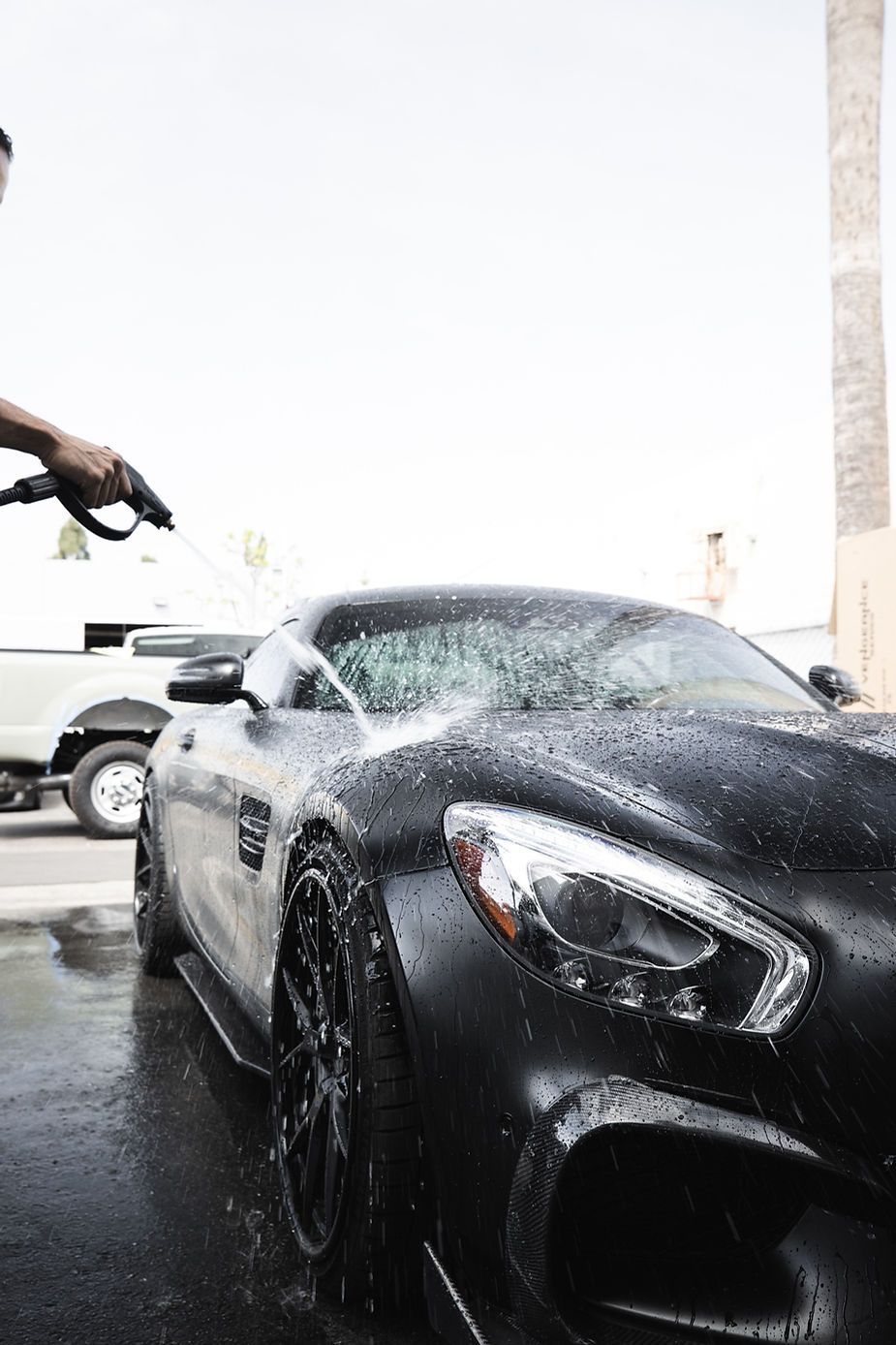 A man is washing a black sports car with a high pressure washer.