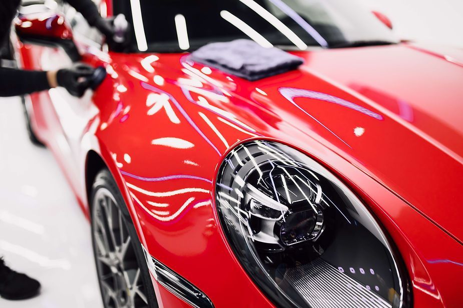 A man is polishing a red car with a microfiber cloth.