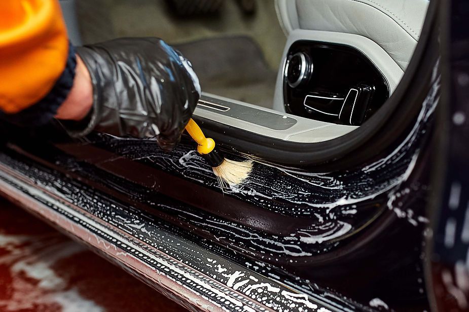 A person is cleaning the side of a car with a brush.