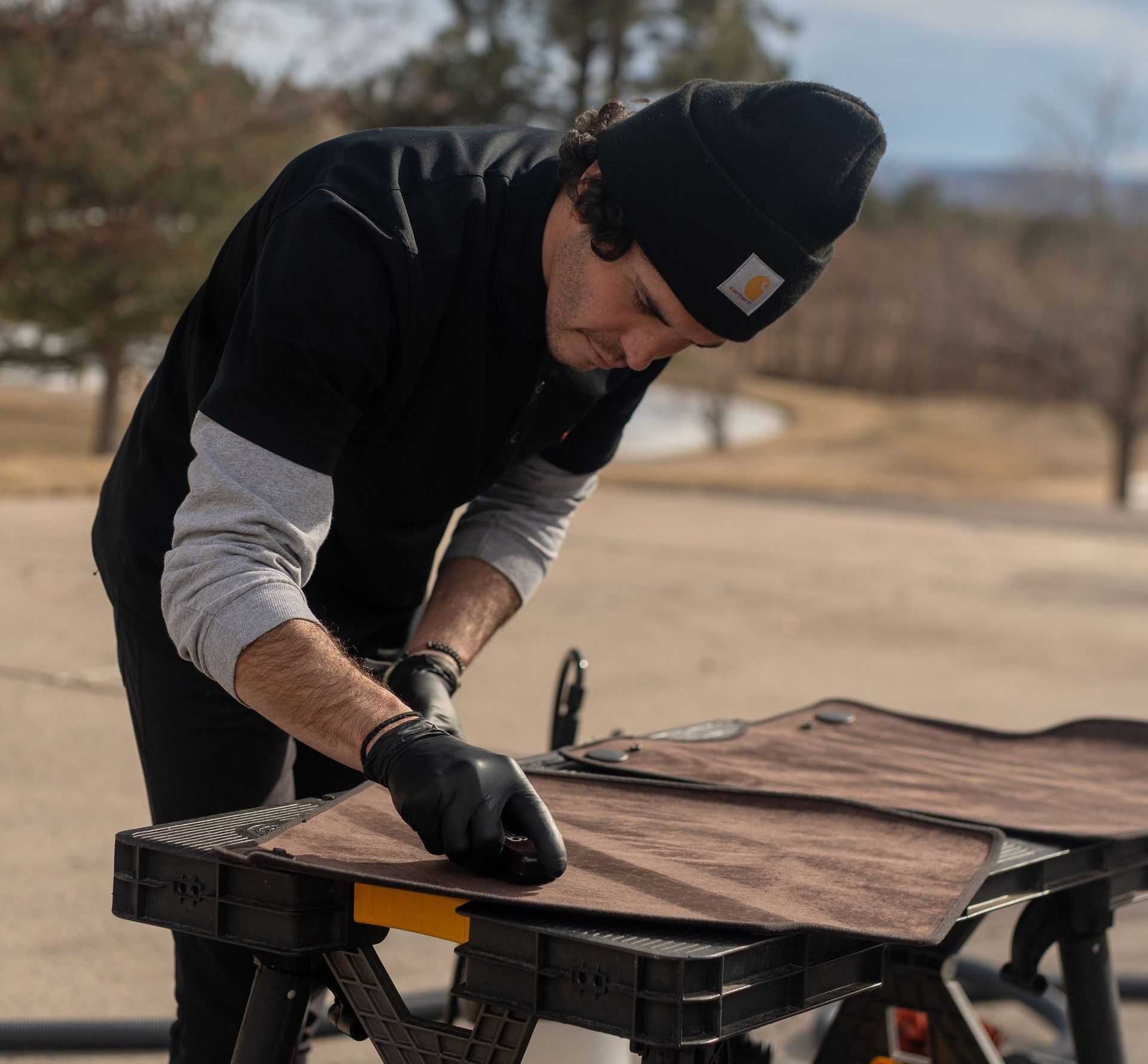 A man wearing a black beanie is working on a piece of wood