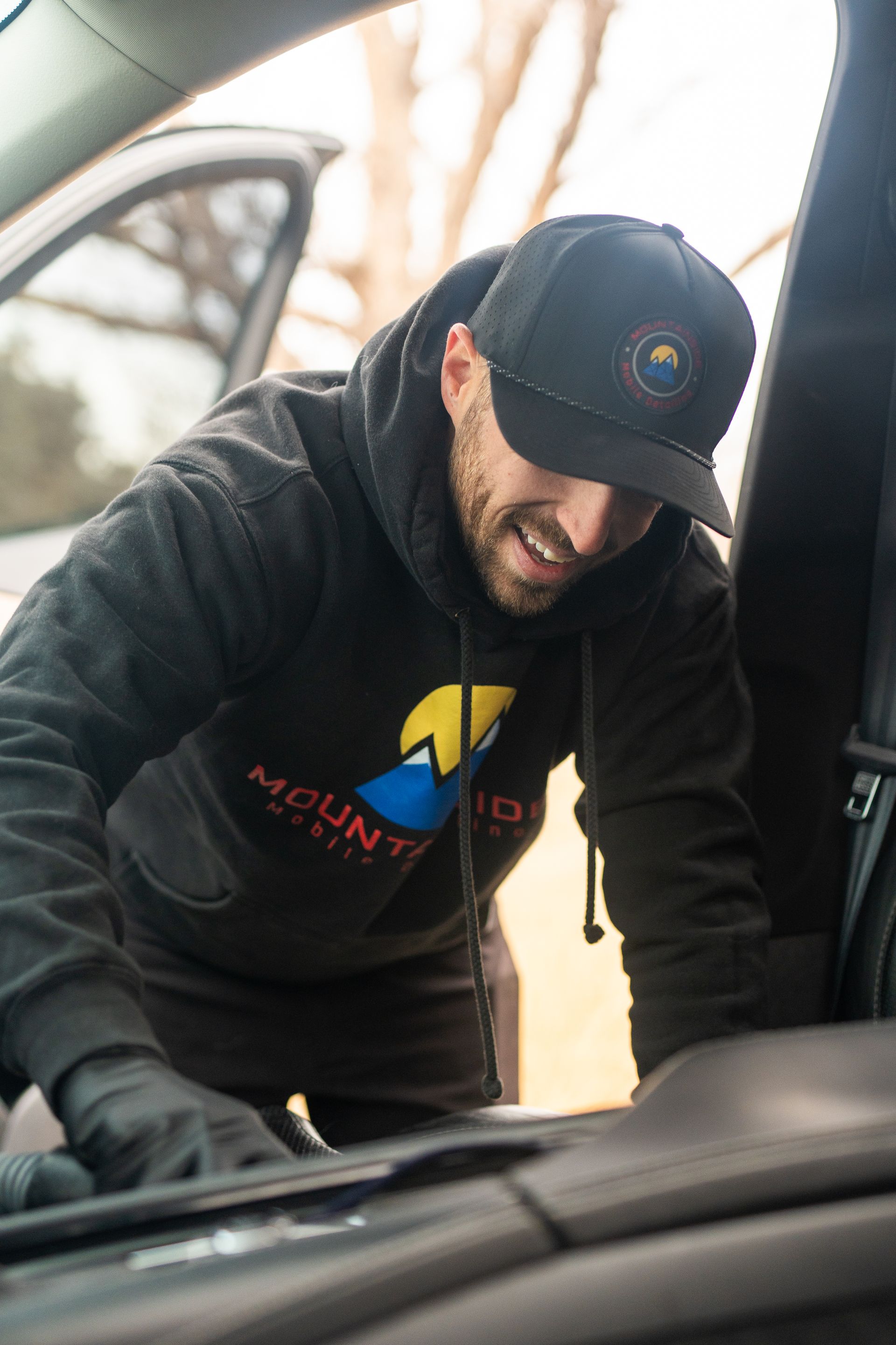 A man wearing a hat and a hoodie is working on a car.