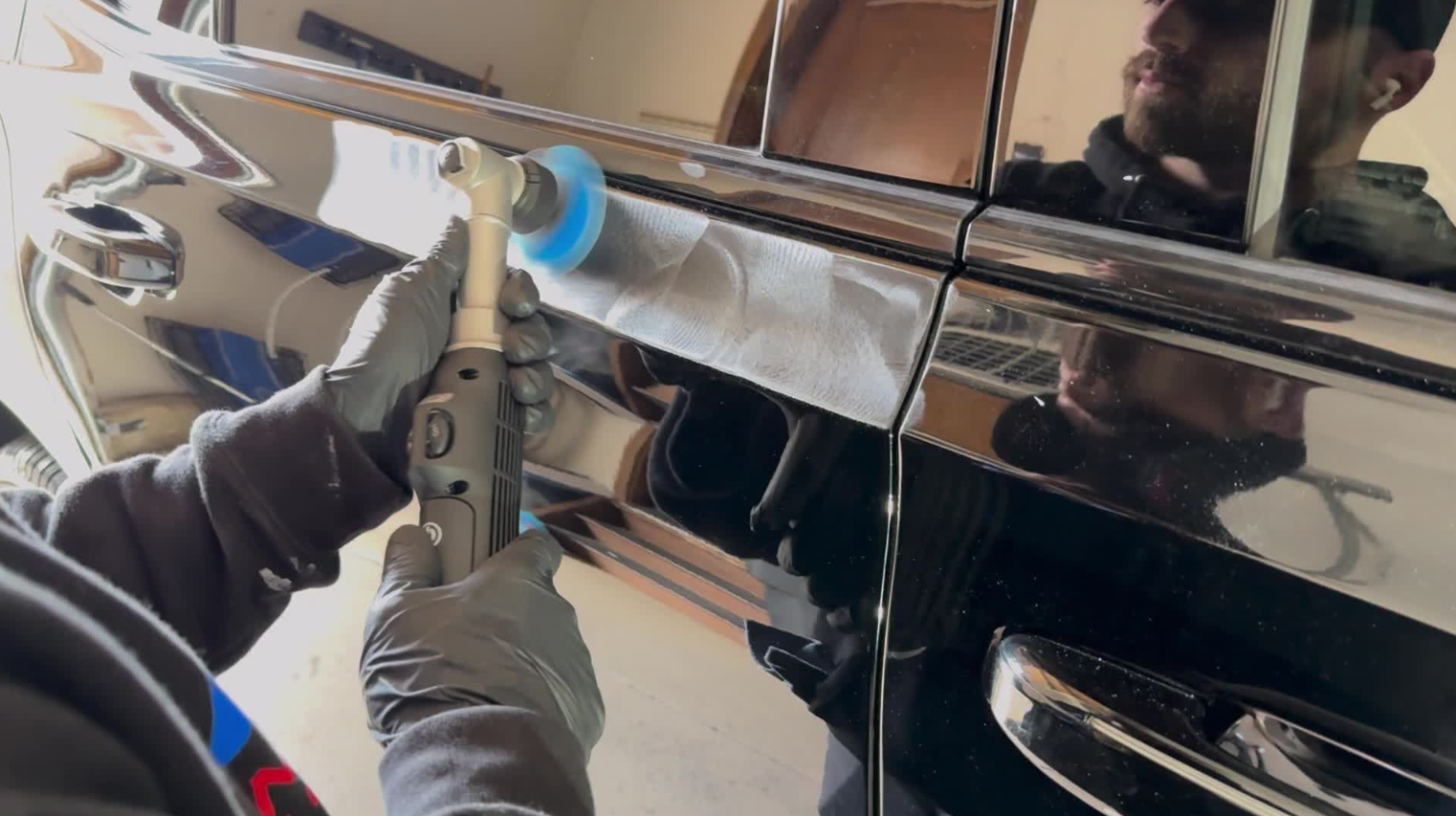 A man is polishing the side of a car with a polisher.