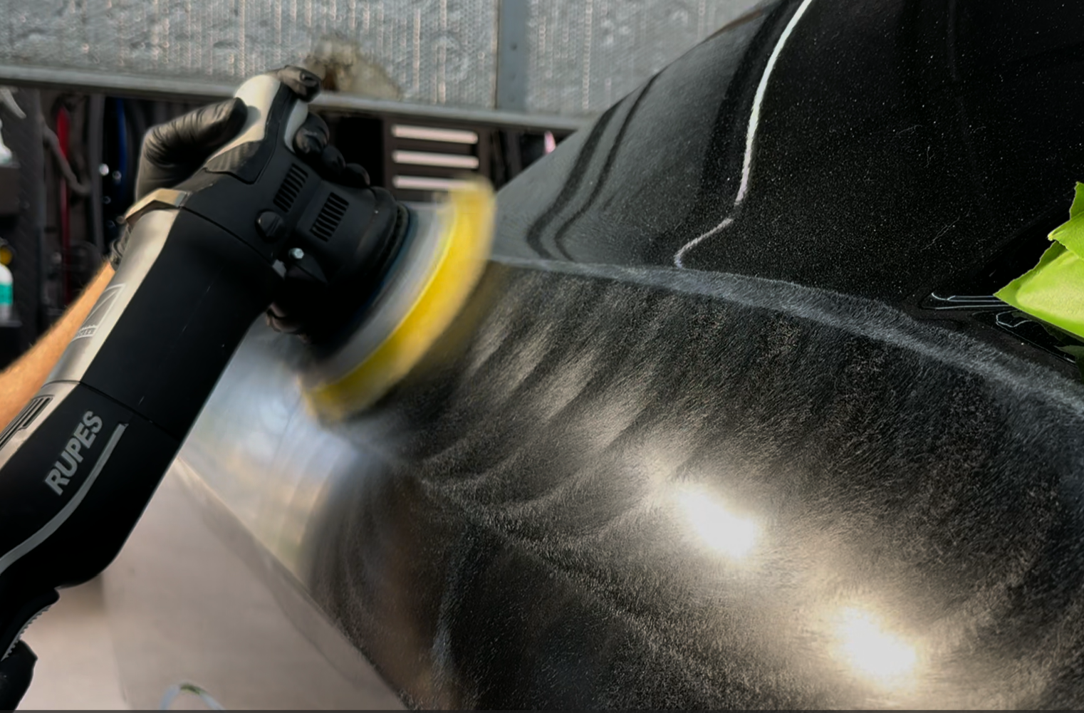A person is polishing a black car with a machine that says rupes