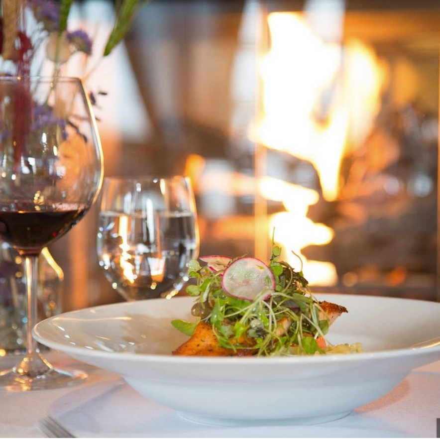 Plate of food with wine glass and fire in background.