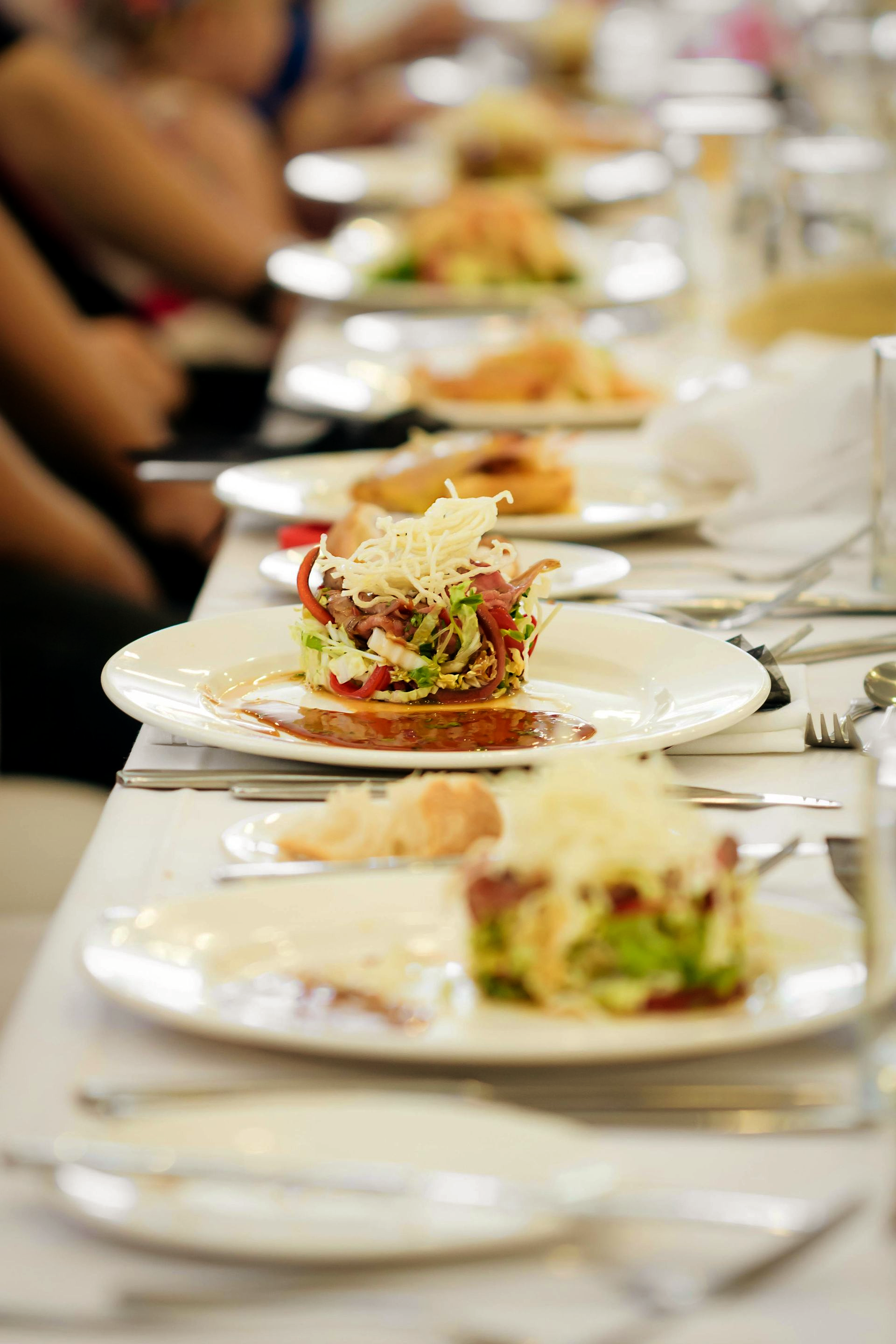 Plated salads with shaved cheese arranged on a long table set for a meal.