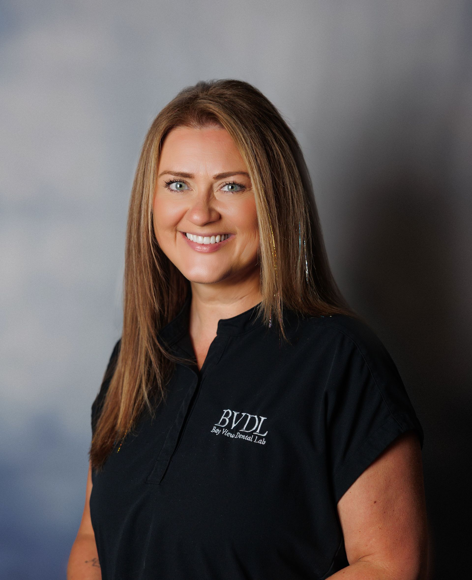 Smiling person in a black shirt standing against a gray studio backdrop