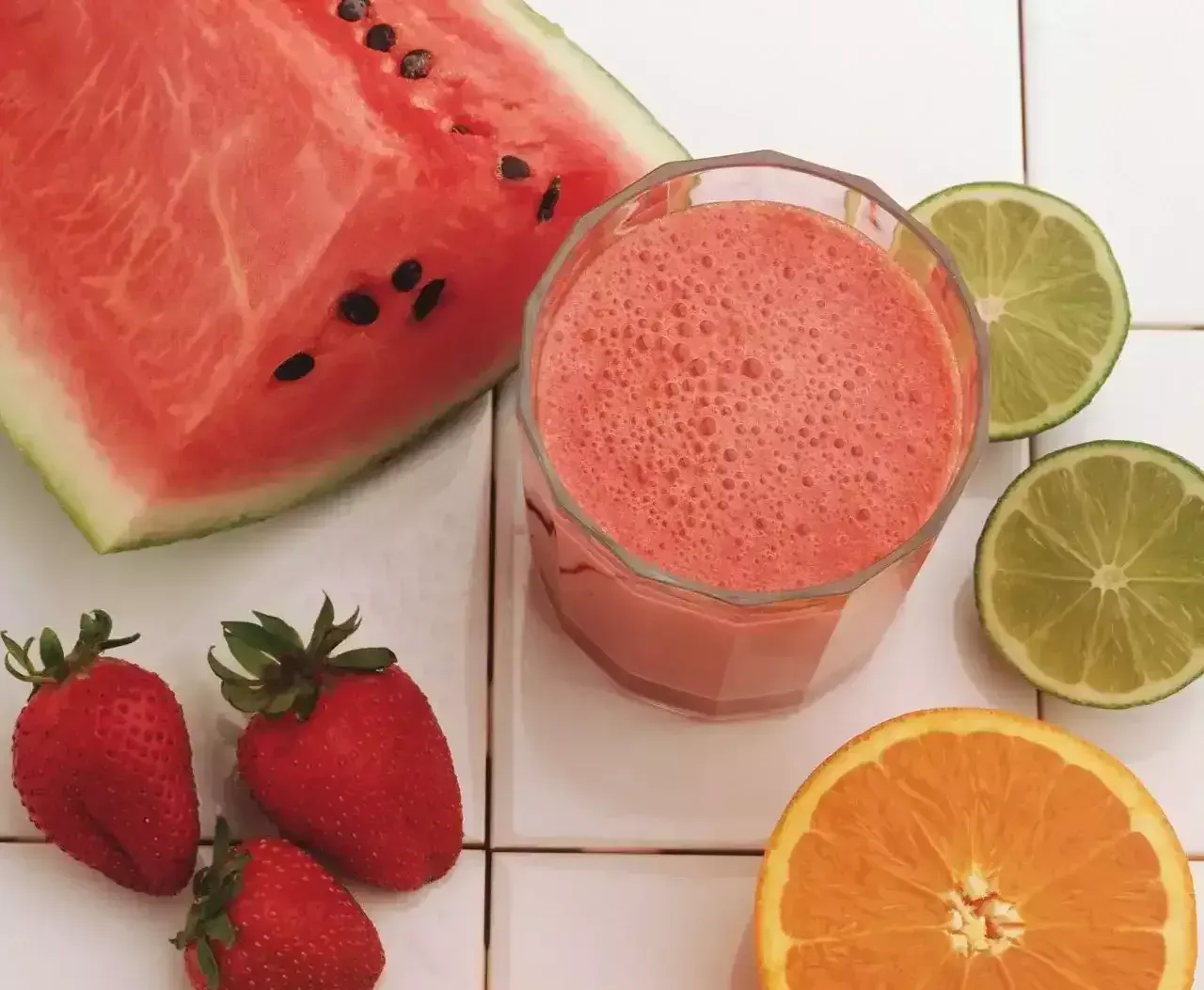 Watermelon smoothie with strawberries, orange, lime, and sliced watermelon on a white background
