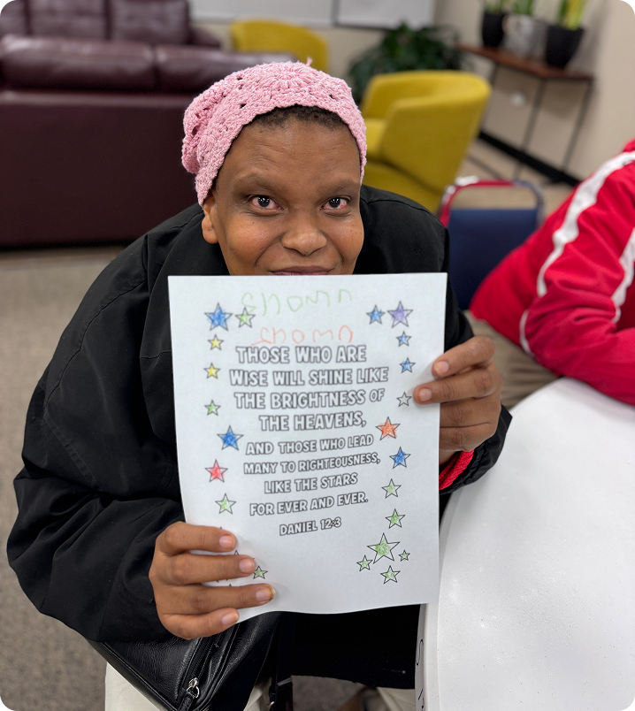 Woman holding a decorated certificate in a classroom, smiling at the camera.