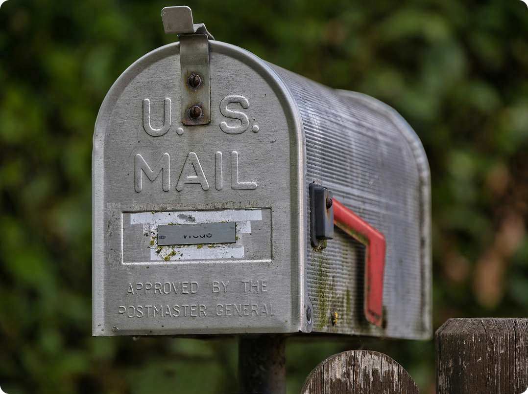 Gray U.S. mailbox with a red flag, mounted on a wooden post outdoors
