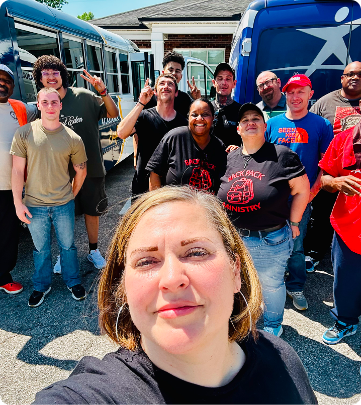 Group selfie outdoors in front of two buses, with several people posing and smiling in bright sunlight