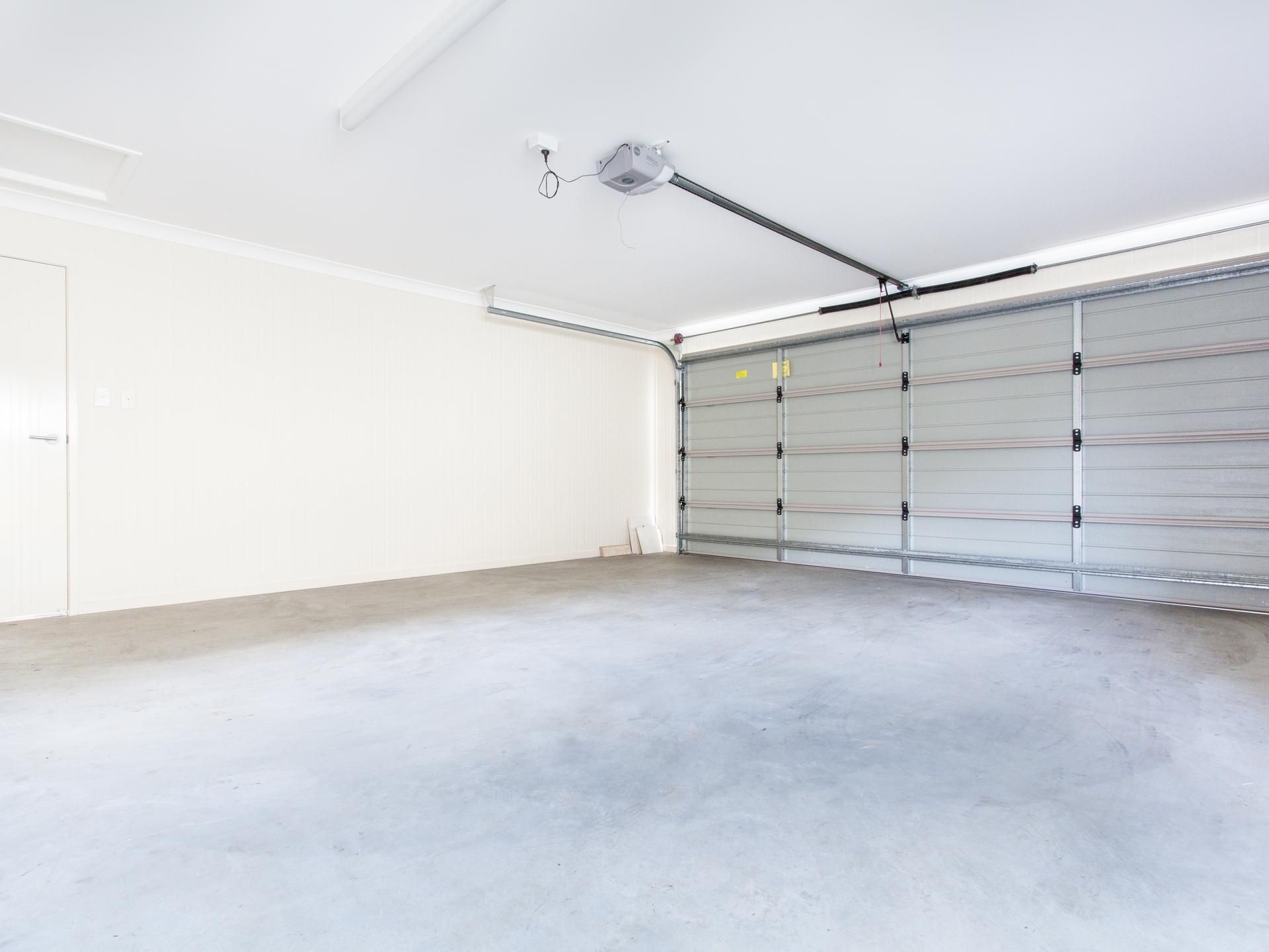Empty garage with a closed, gray sectional door. Concrete floor, white walls and ceiling.