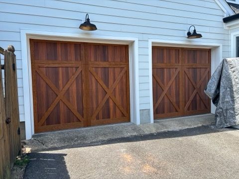 Two wooden garage doors with X-brace panels on a light blue house exterior.