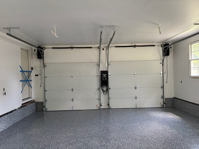 Empty two-car garage with white doors, gray epoxy floor, and side window.