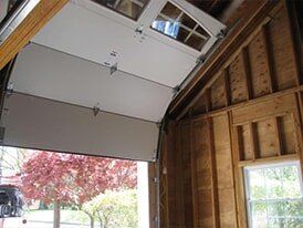 White garage door partially open, revealing a red tree. Wooden interior visible.