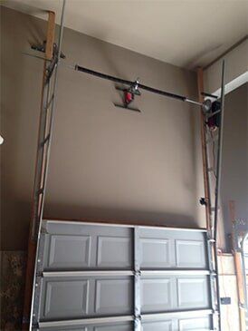 Garage door with opener installed, against a tan wall, with metal tracks and supports.