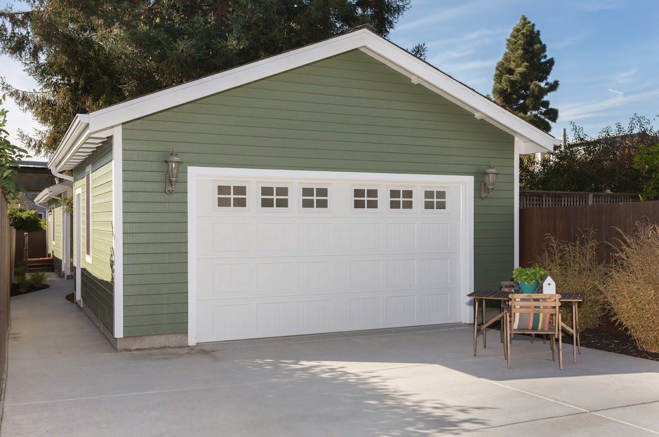 Green garage with white garage door, concrete driveway, and small table.