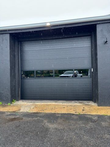 Closed black garage door on a dark building exterior with a narrow horizontal window.