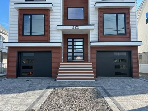 Modern townhouse front facade with two black garage doors, central stairs, and paved driveway