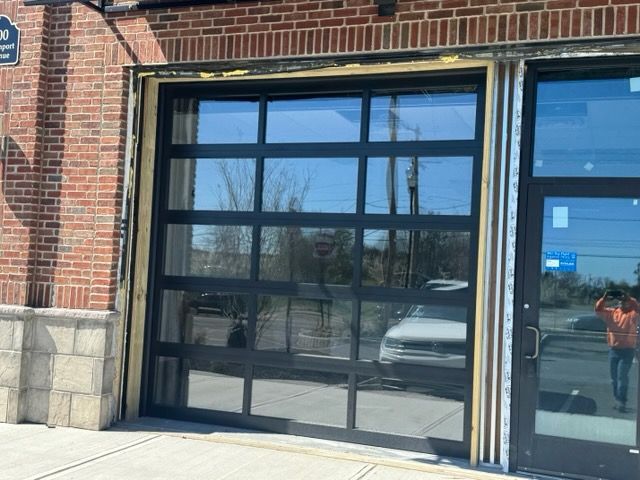 Brick building entrance with black glass garage door and stone base, reflecting a parked white vehicle.