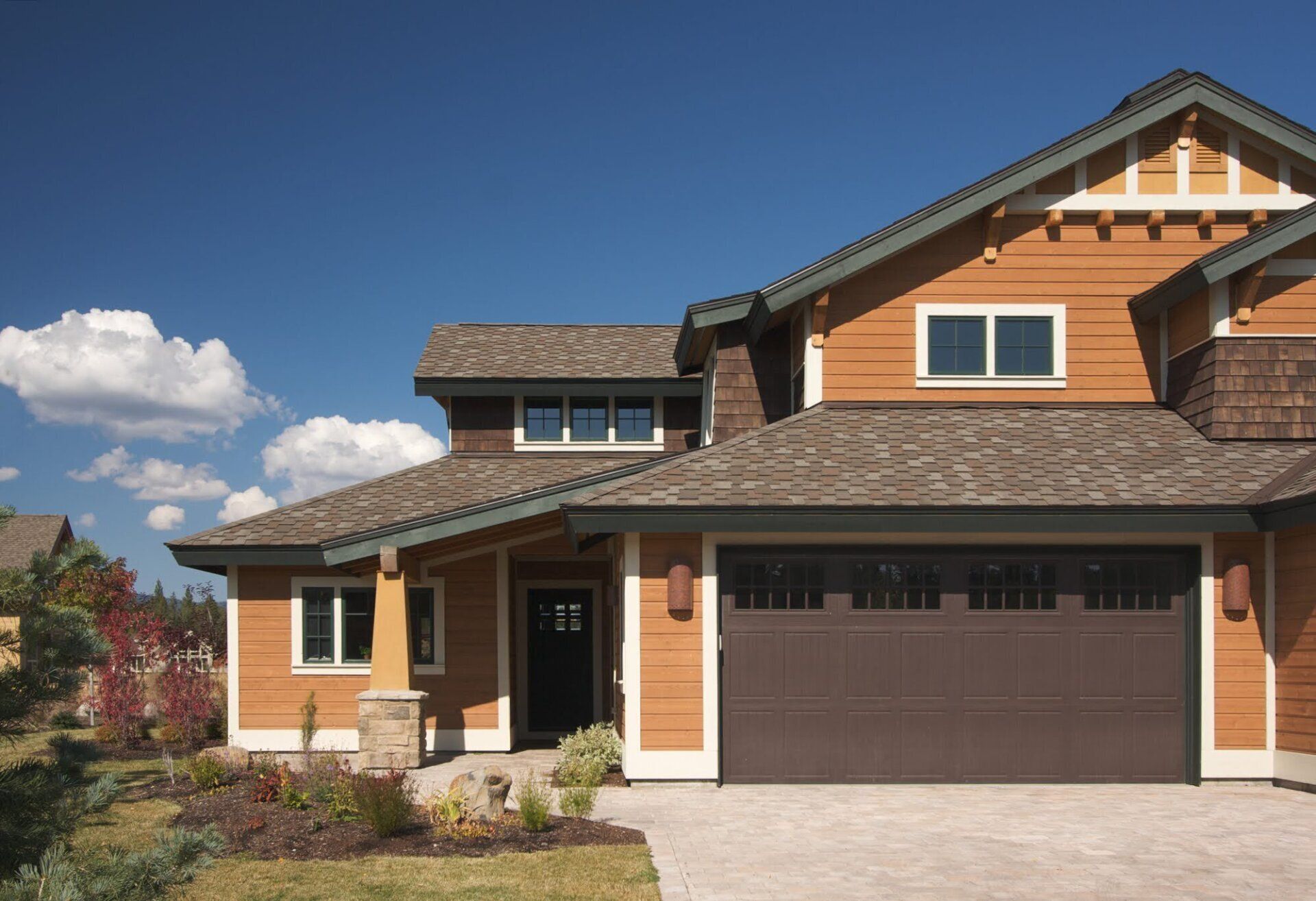 Orange two-story house with brown garage door, windows, and roof against a blue sky with clouds.