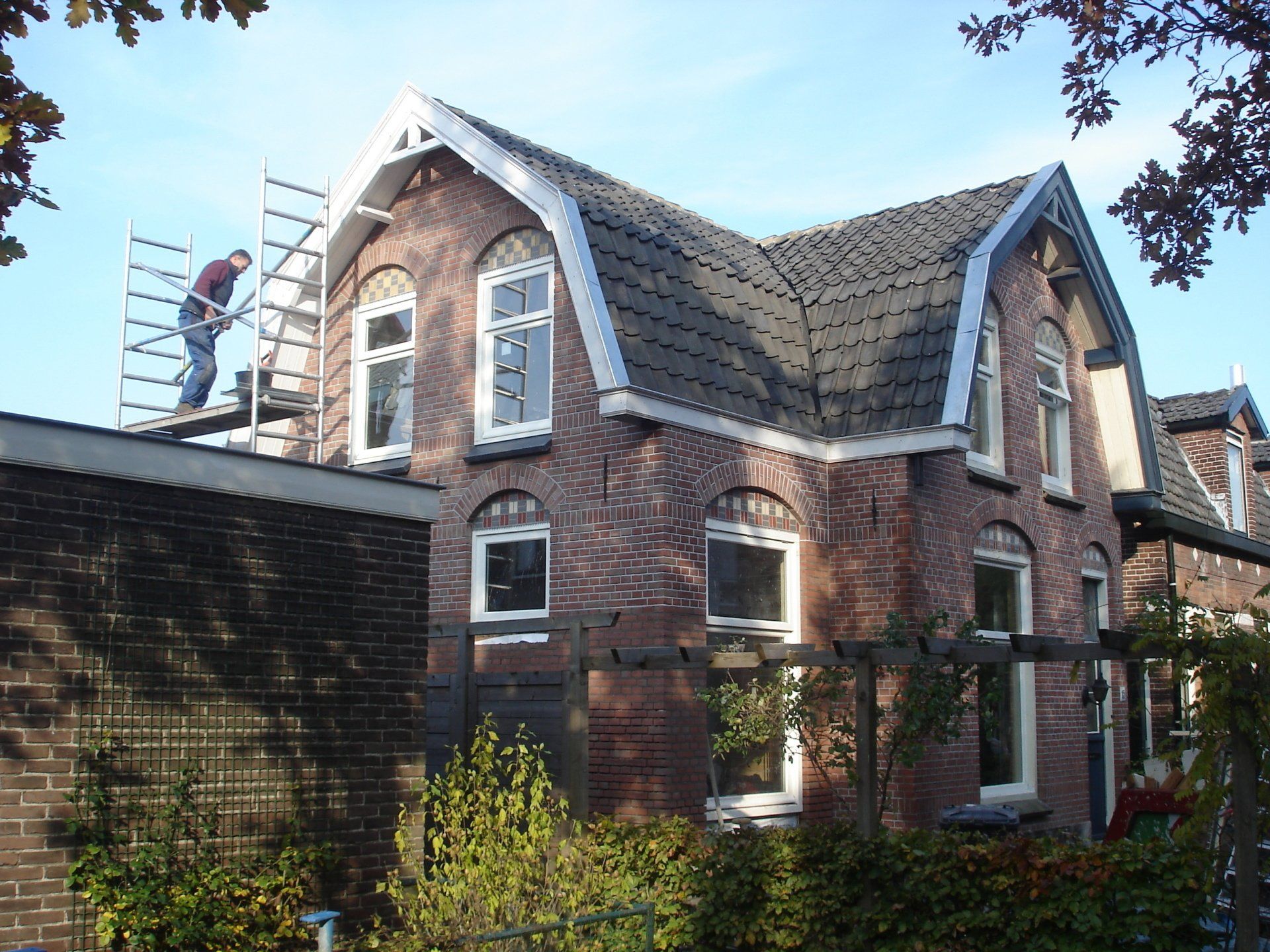 Brick house with a man on a scaffolding, working on the roof in a sunny, outdoor setting.