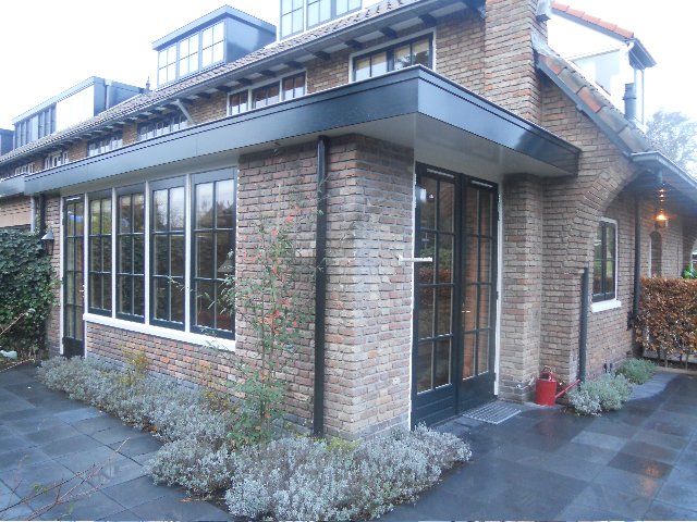 Brick house with large windows and black trim, small garden bed, and blue-gray paving stones.