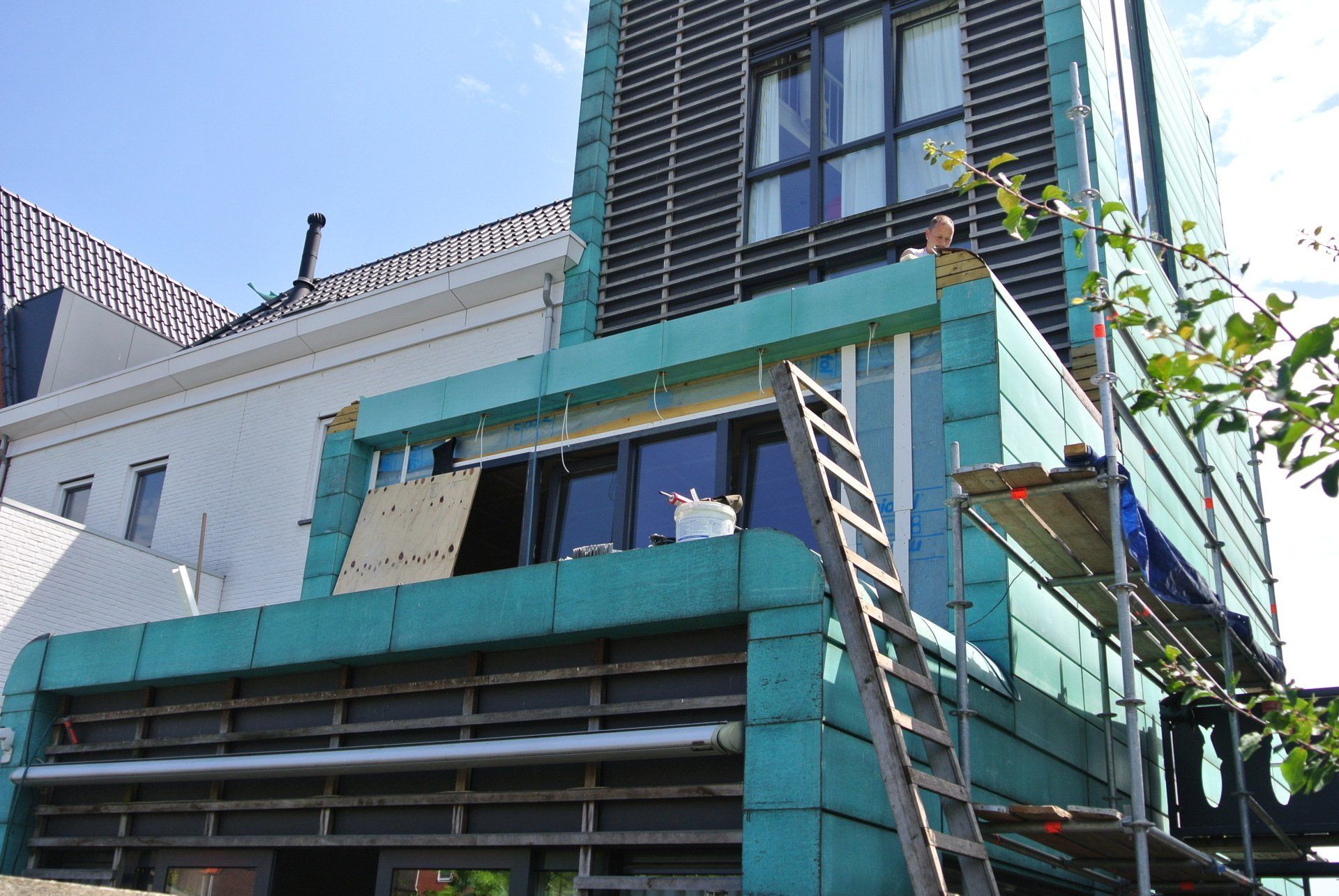 Building exterior with green and black facade, scaffolding, and a person working on the roof.
