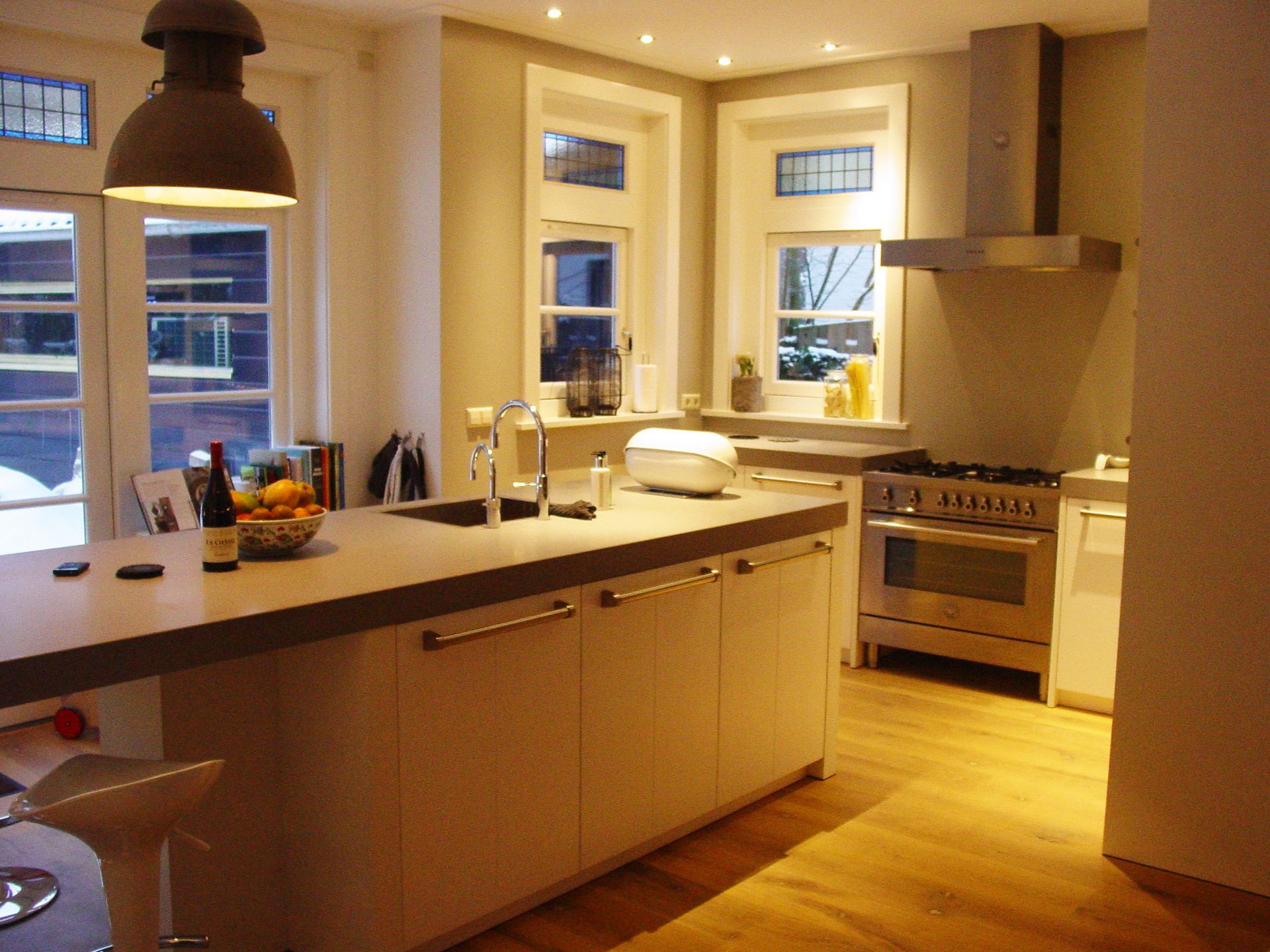 Kitchen with island, stainless steel appliances, and large windows, with light wood floors and neutral paint.