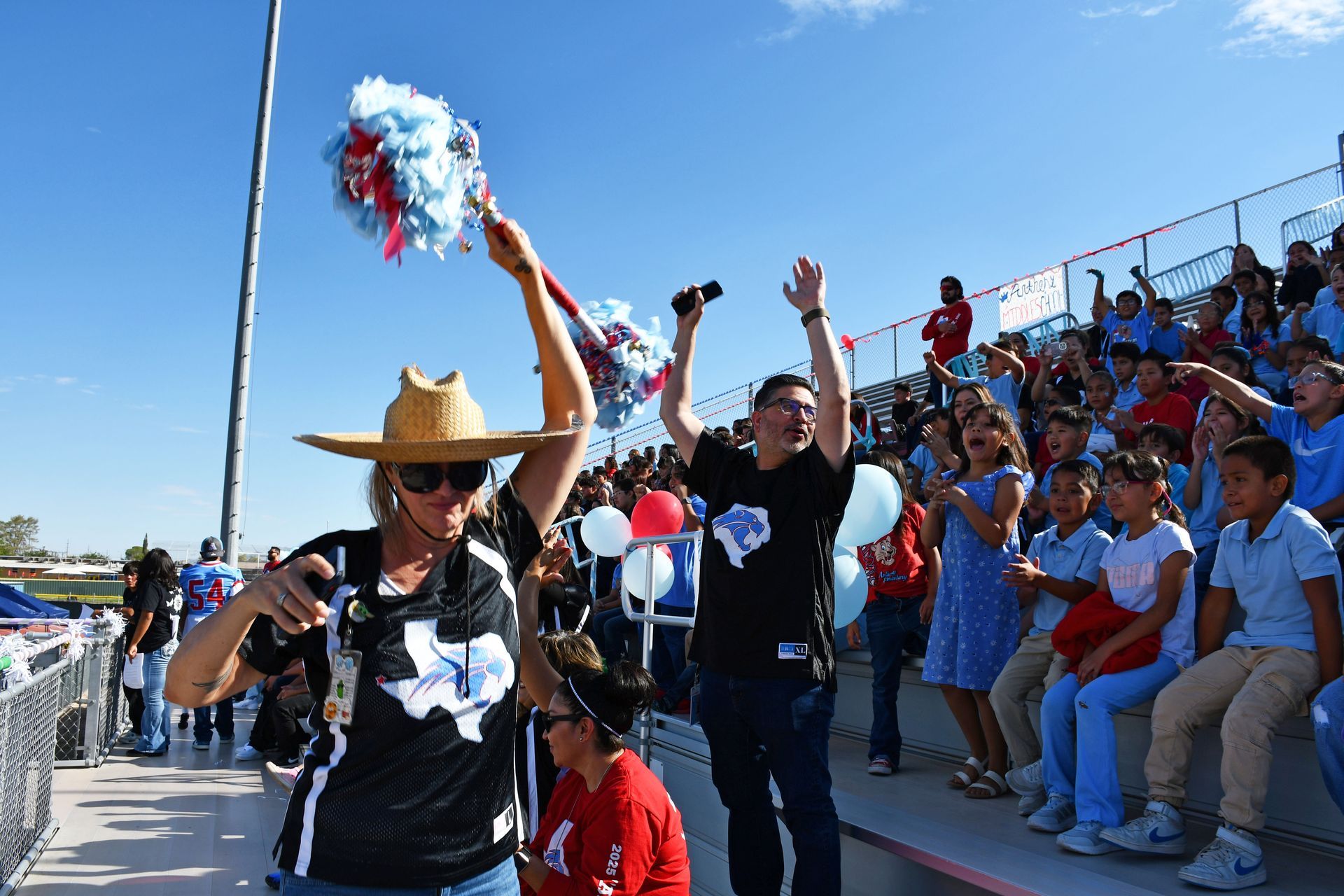School counselor holds  red and blue spirit stick while students cheer on the football bleachers during back-to-school peprally.