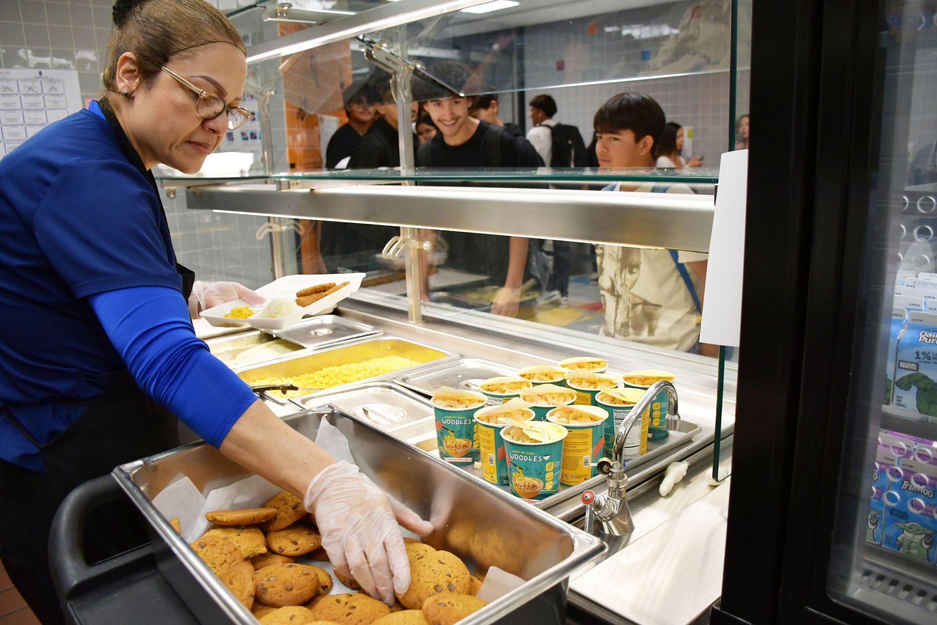 Child Nutrition Department employee reaches for cookies as she assembles plate for students during lunchtime.