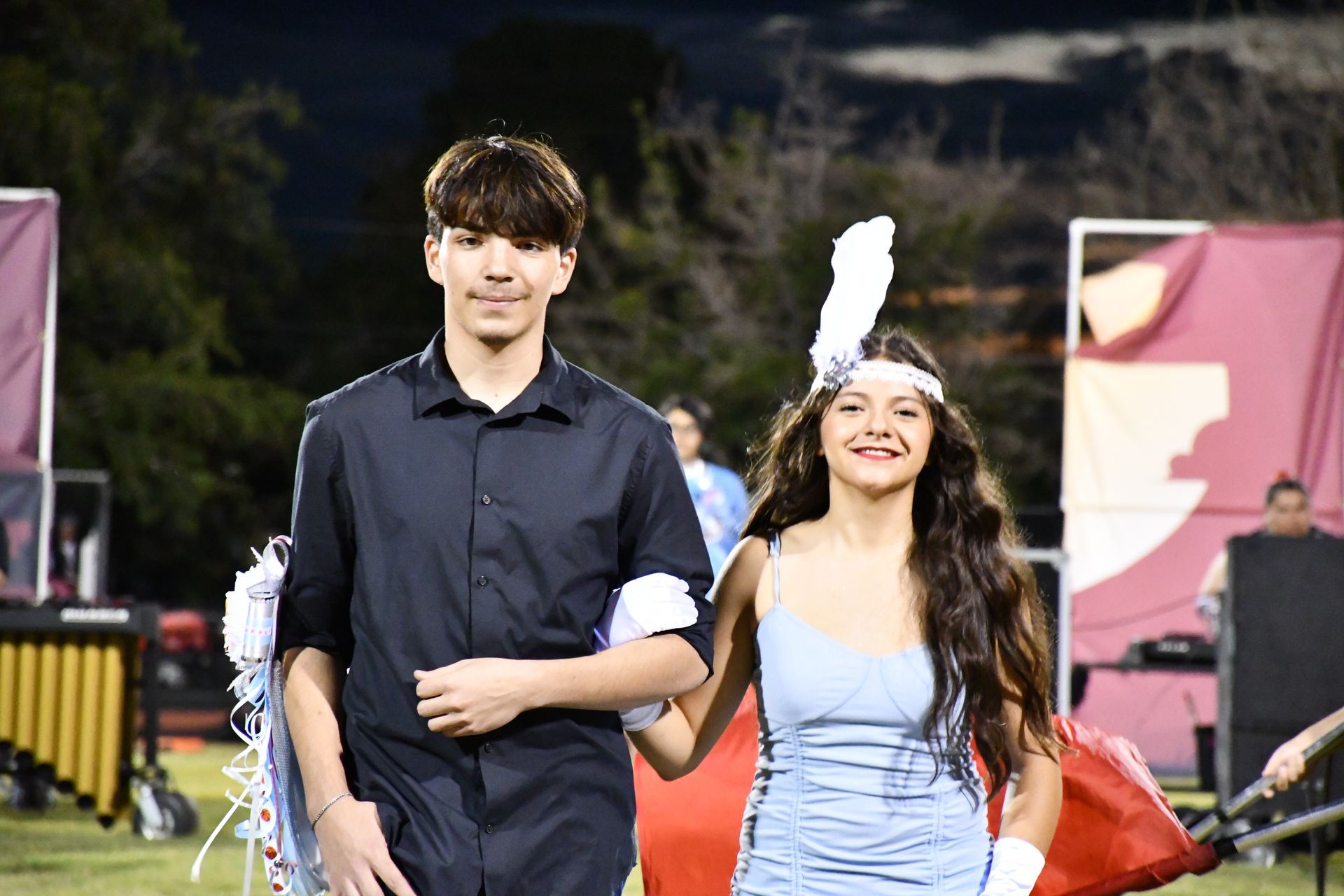 Female student is escorted down the football field during homecoming. She is wearing a feather on her head in the casino homecoming theme