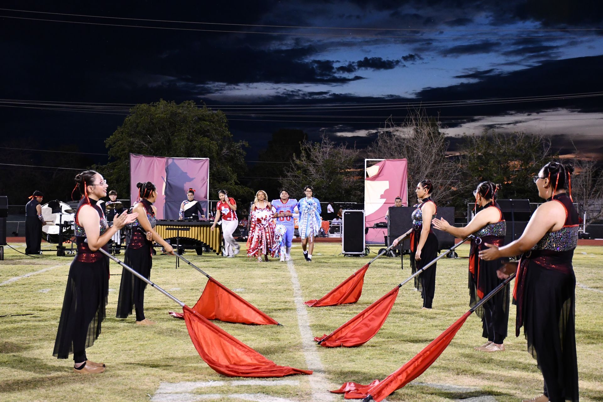 Colorguard girls hold red flags as homecoming queen and king nominees walk down football field