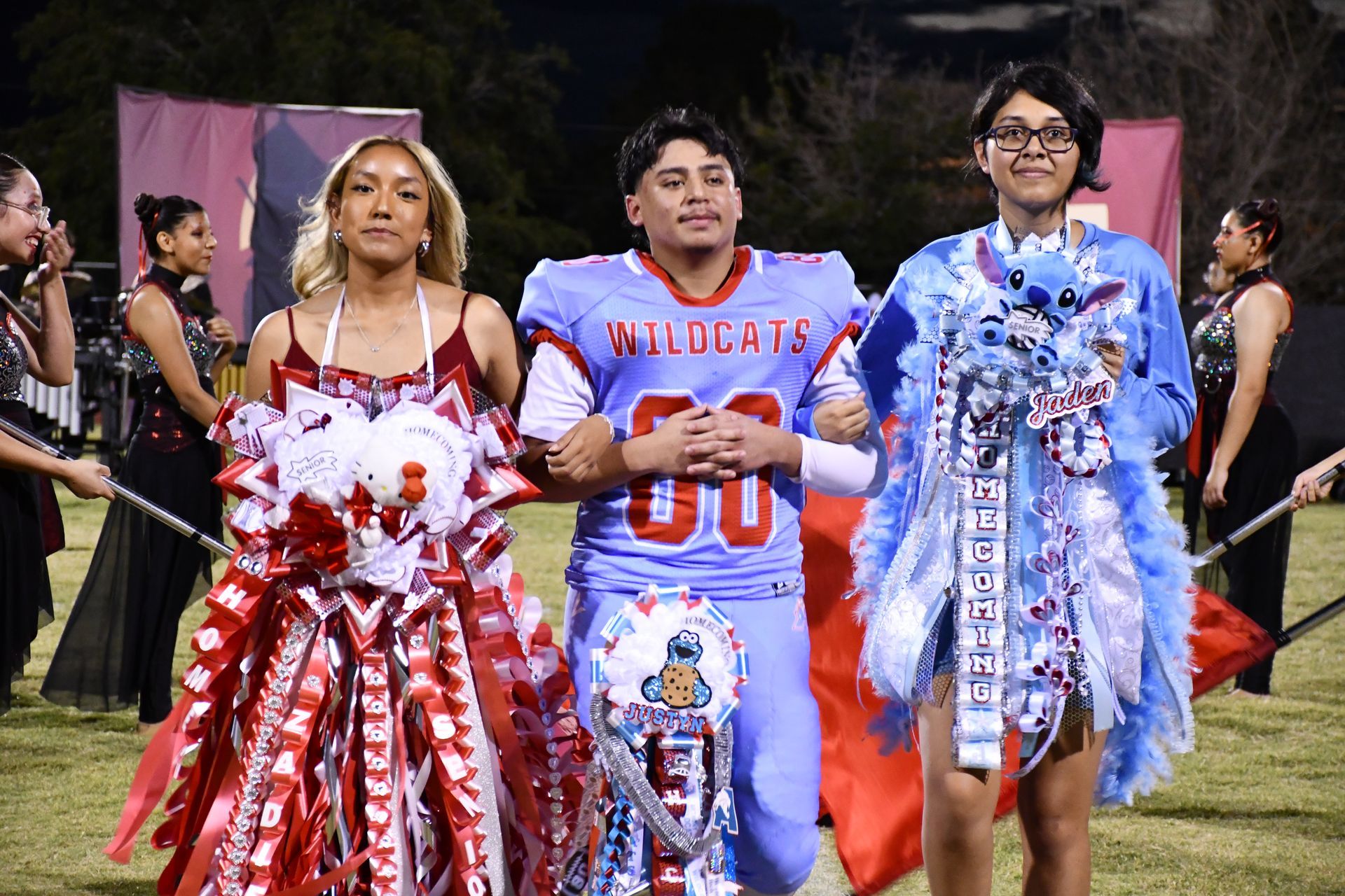 Two female students are walked down the football field by a male student. The three of them were nominated for Homecoming Queen and King
