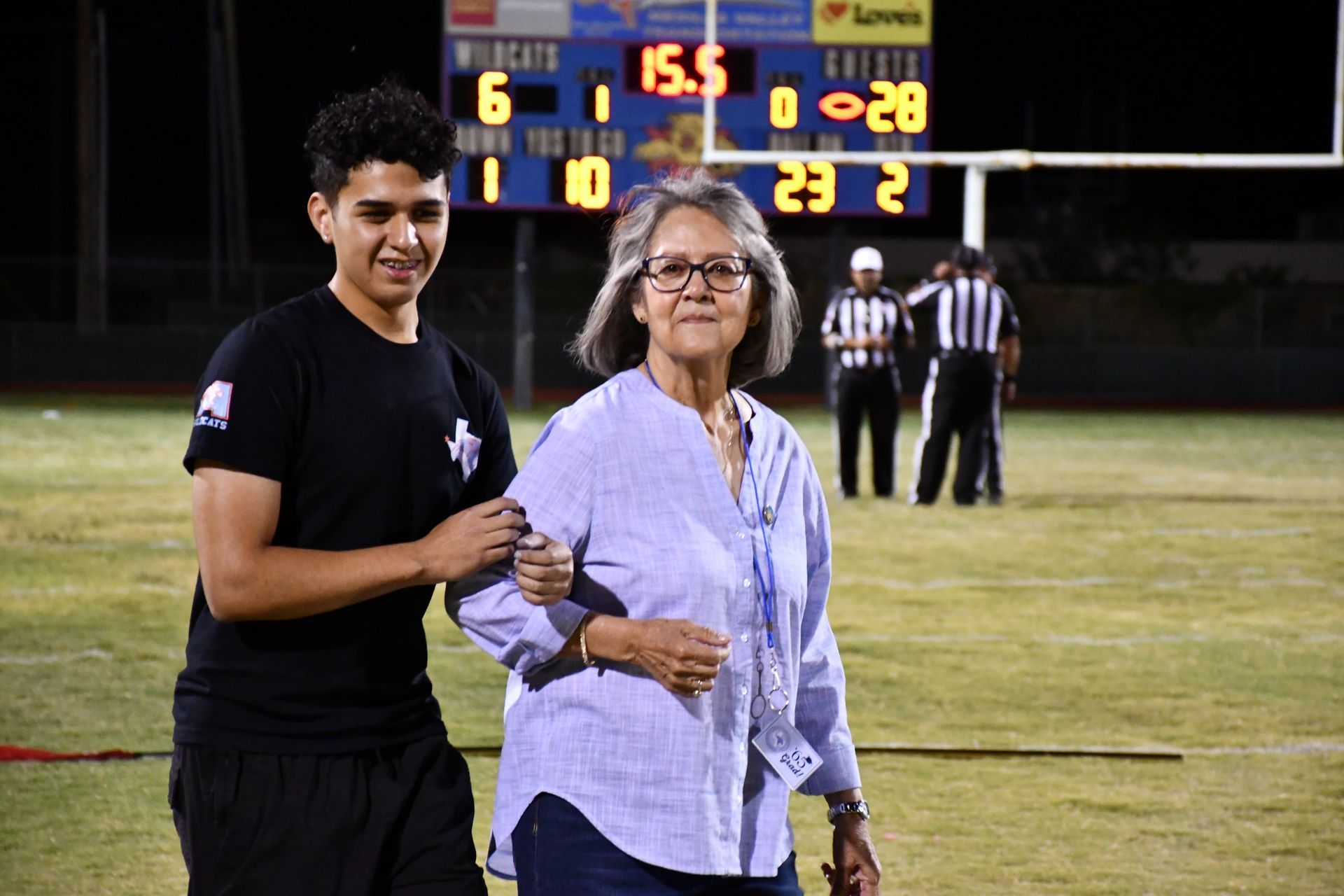 Male student holds the arm of a woman as they walk onto the football field.