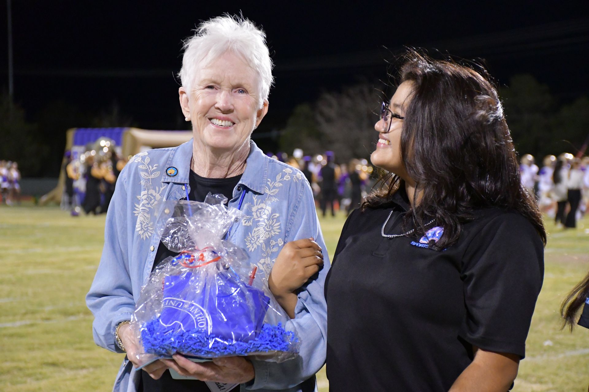 Woman smiles at camera while holding a gift basket. Student looks at woman and smiles.